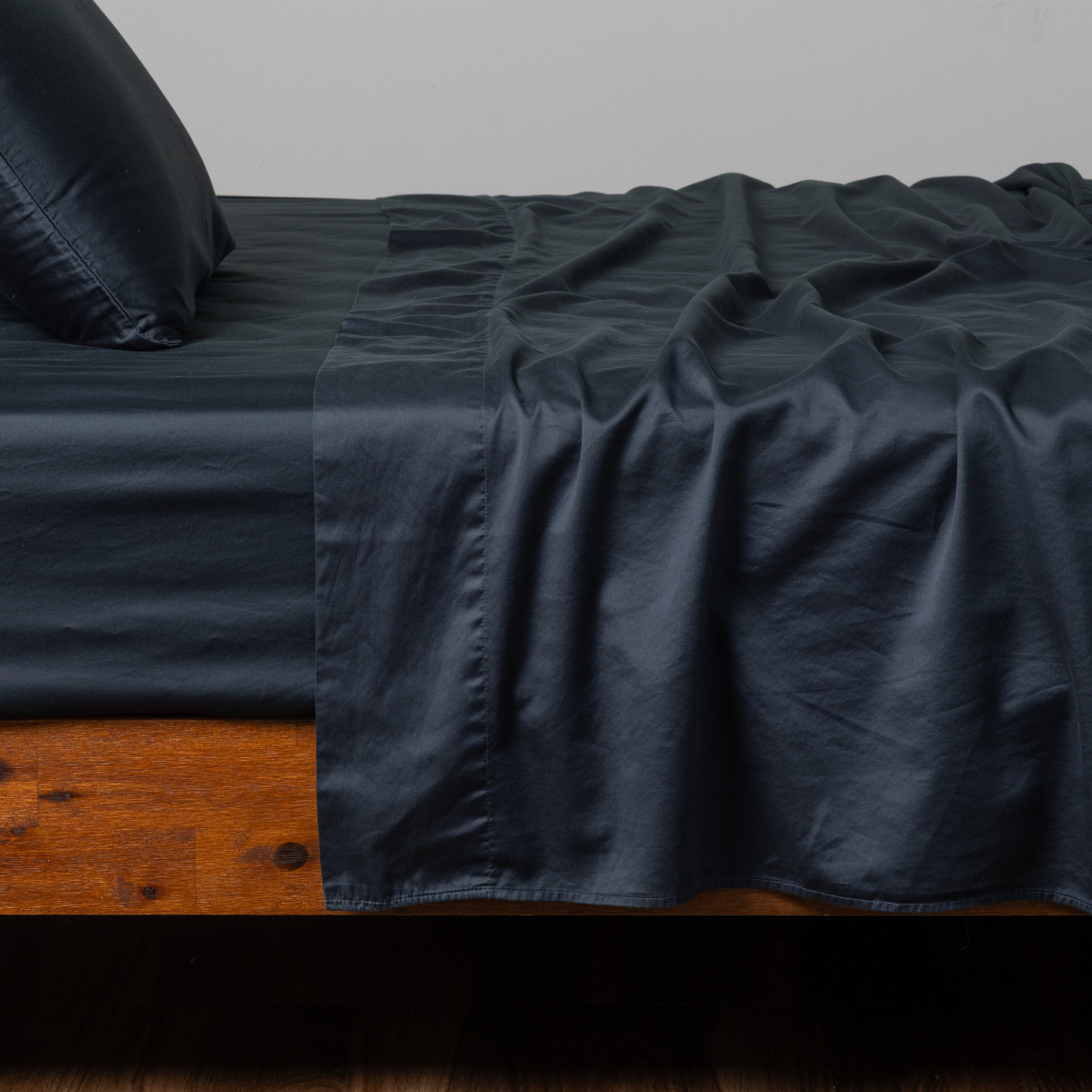 Slate flat sheet draped loosely over a wood-frame bed with matching pillowcase.