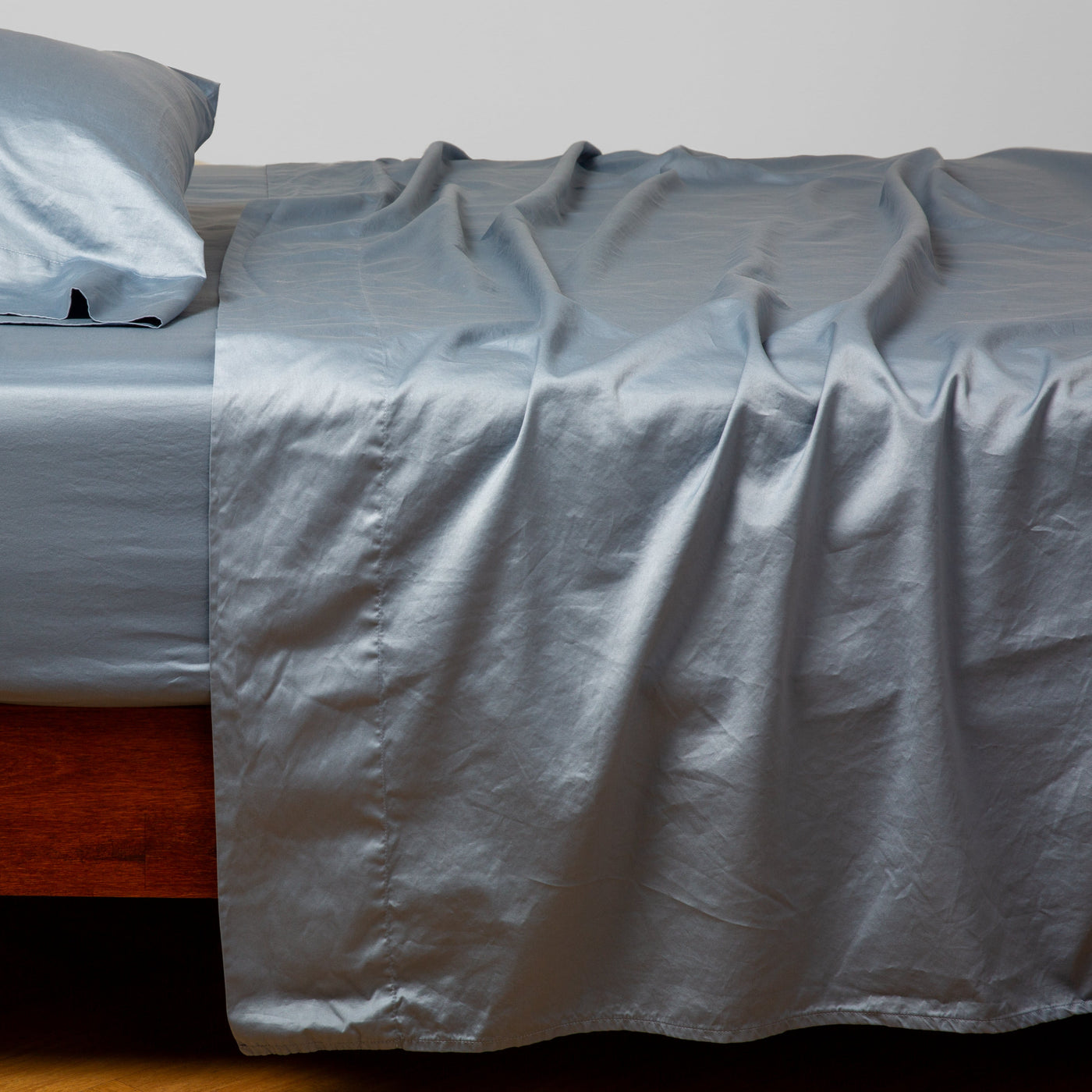 Bria fitted sheet in Tahoe Blue draped loosely over a wood-framed bed with matching pillowcase.