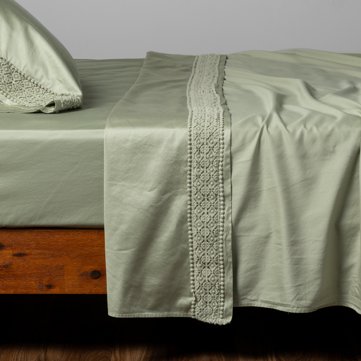 Desert Sage flat sheet draped over bed, showing wide crochet lace trim detail along folded edge.