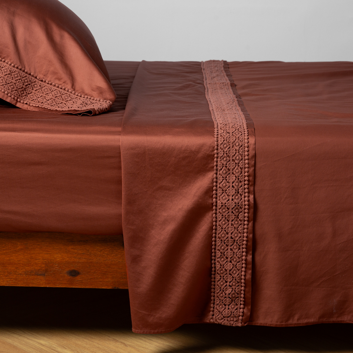 Flat sheet detail showing Autumn lace trim band against smooth sateen, styled on bed with matching pillowcase.
