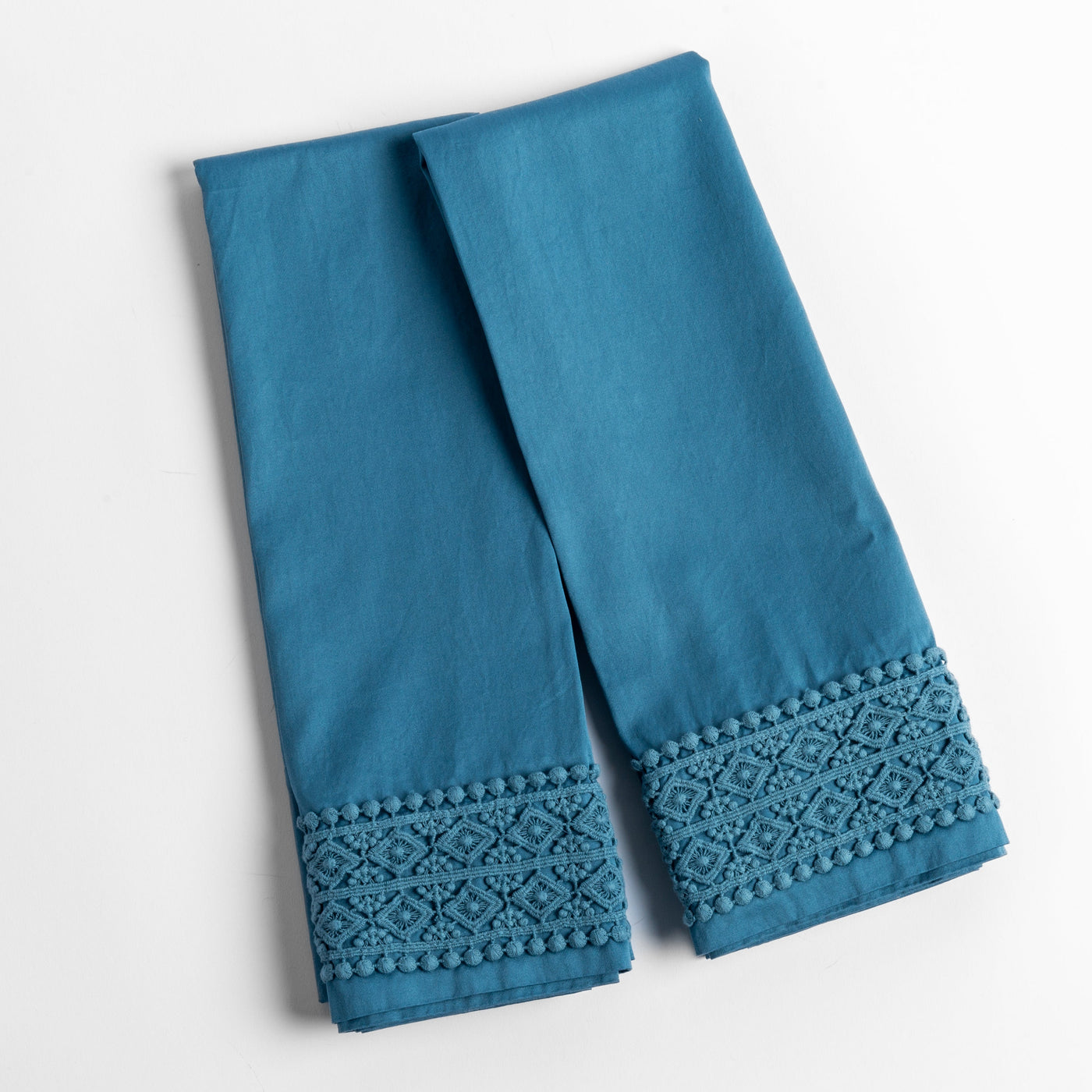Cenote pillowcase hem detail showing geometric lace trim and pom-pom border.