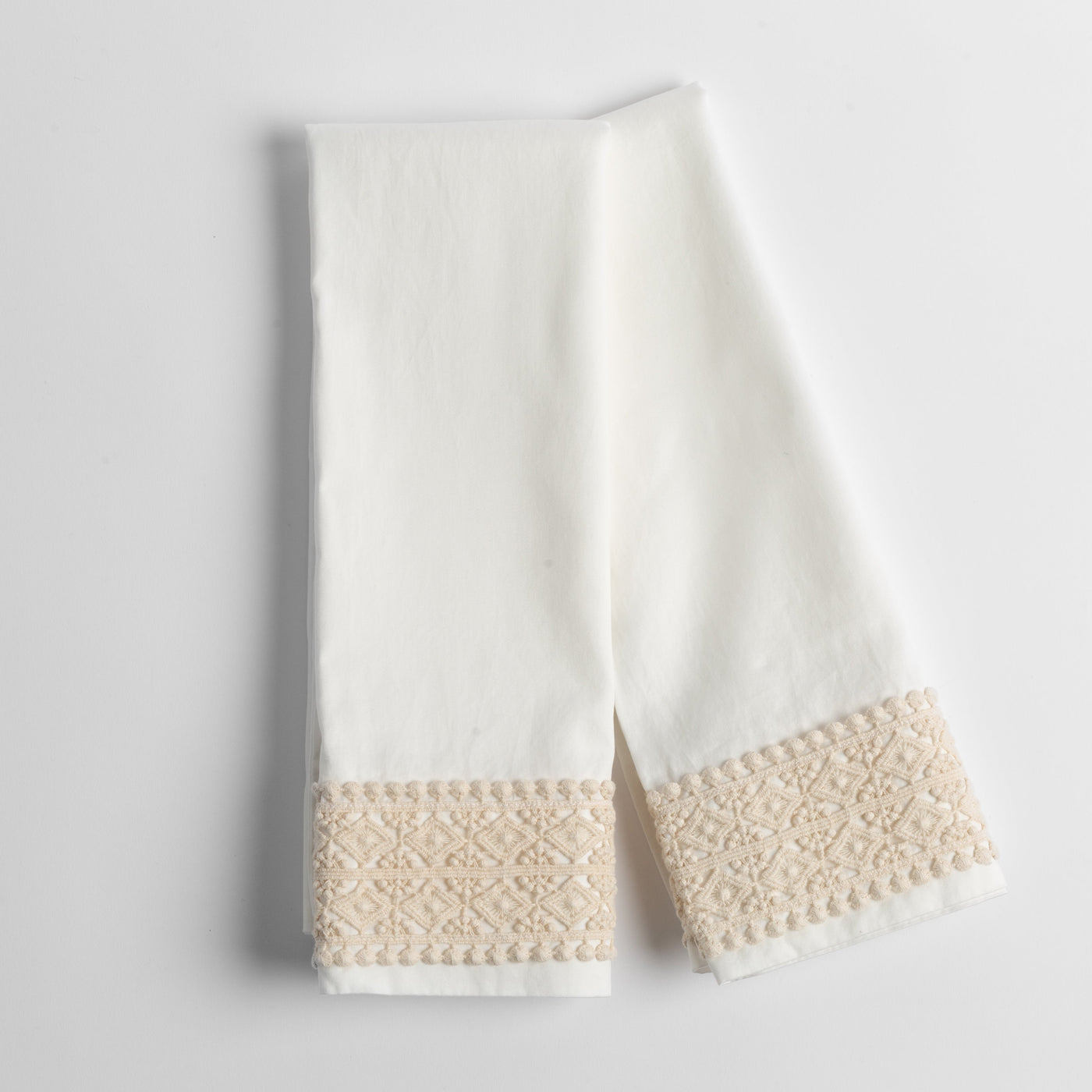 Close-up of Winter White pillowcase hem with textured champagne geometric embroidered border trim.