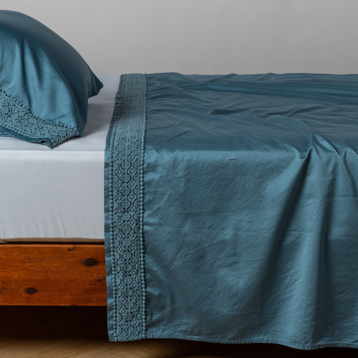 Cenote flat sheet draped over bed, geometric lace trim along border with matching pillowcase.