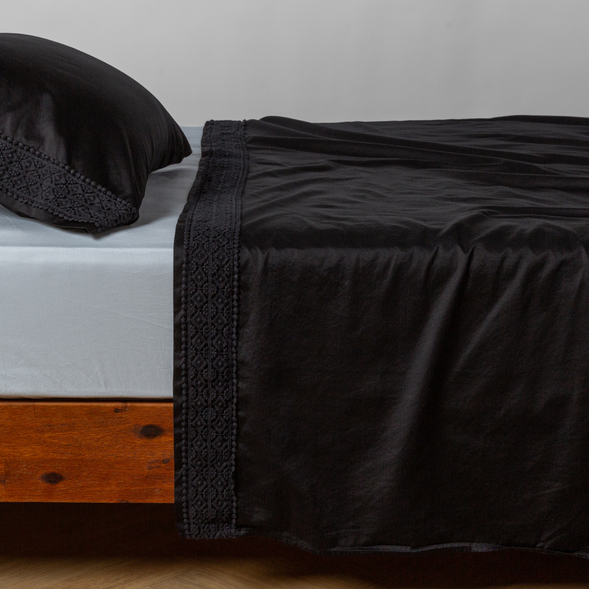 Corvino flat sheet draped over bed, showing geometric lace trim detail along top hem.