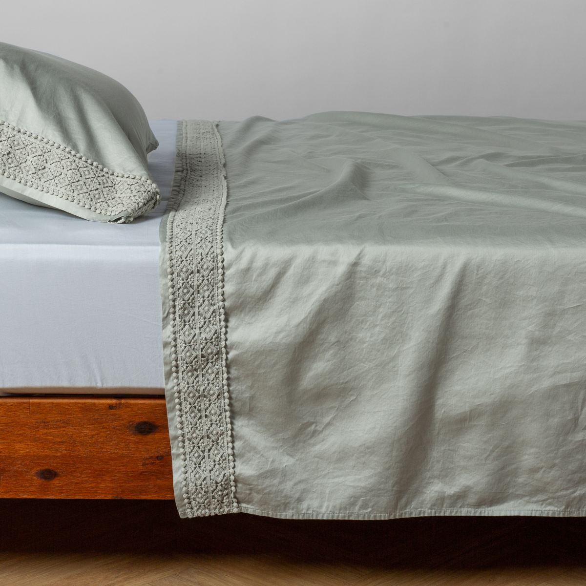 Lace trim detail on Eucalyptus flat sheet folded over bed with matching pillowcase.