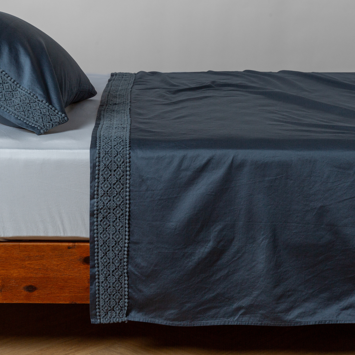 Midnight flat sheet draped over bed, showing wide lace-trim border detail with matching pillowcase.