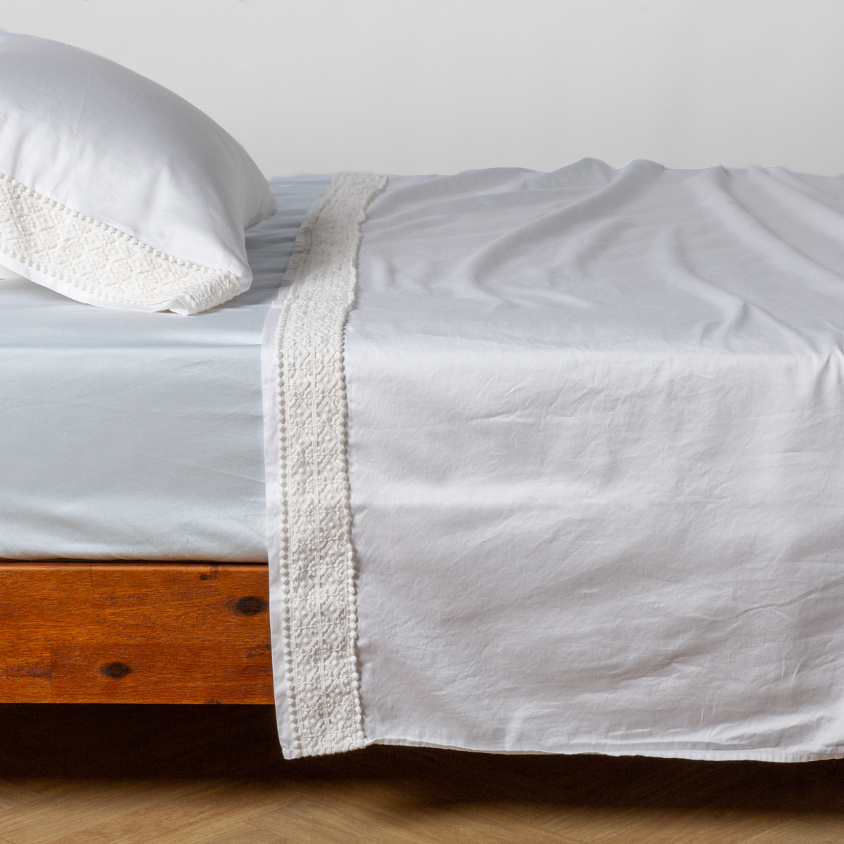 White flat sheet with wide crochet lace trim border, draped over a wood-frame bed.