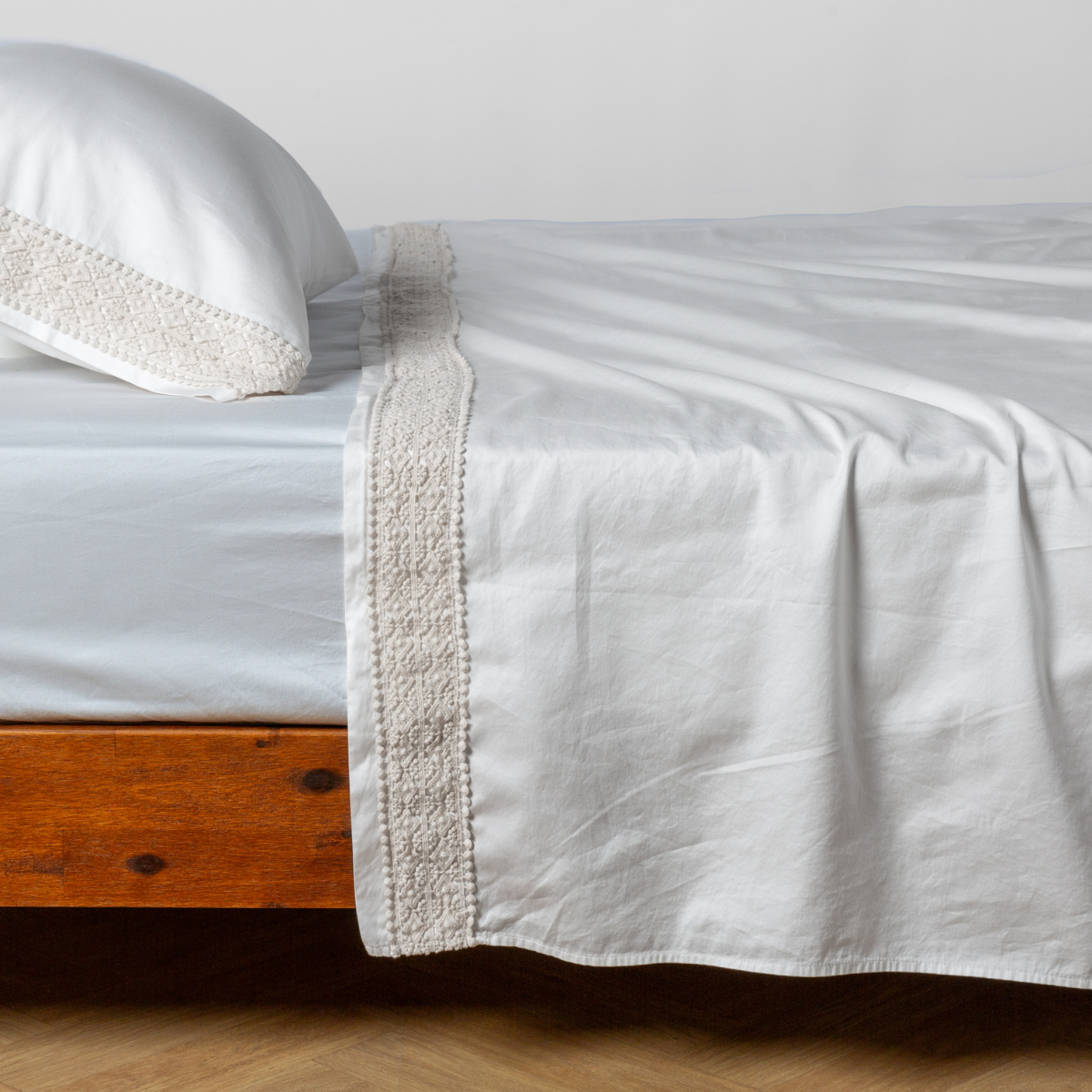 Bella Notte Bria flat sheet in Winter White, lace trim detail draped over bed.