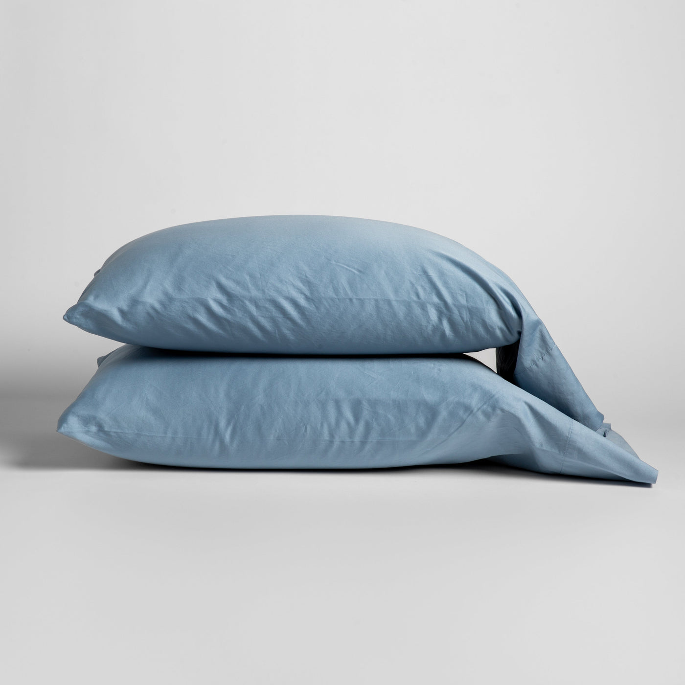 Two Bella Notte Bria pillowcases stacked in Tahoe Blue, soft cotton, against a neutral background.