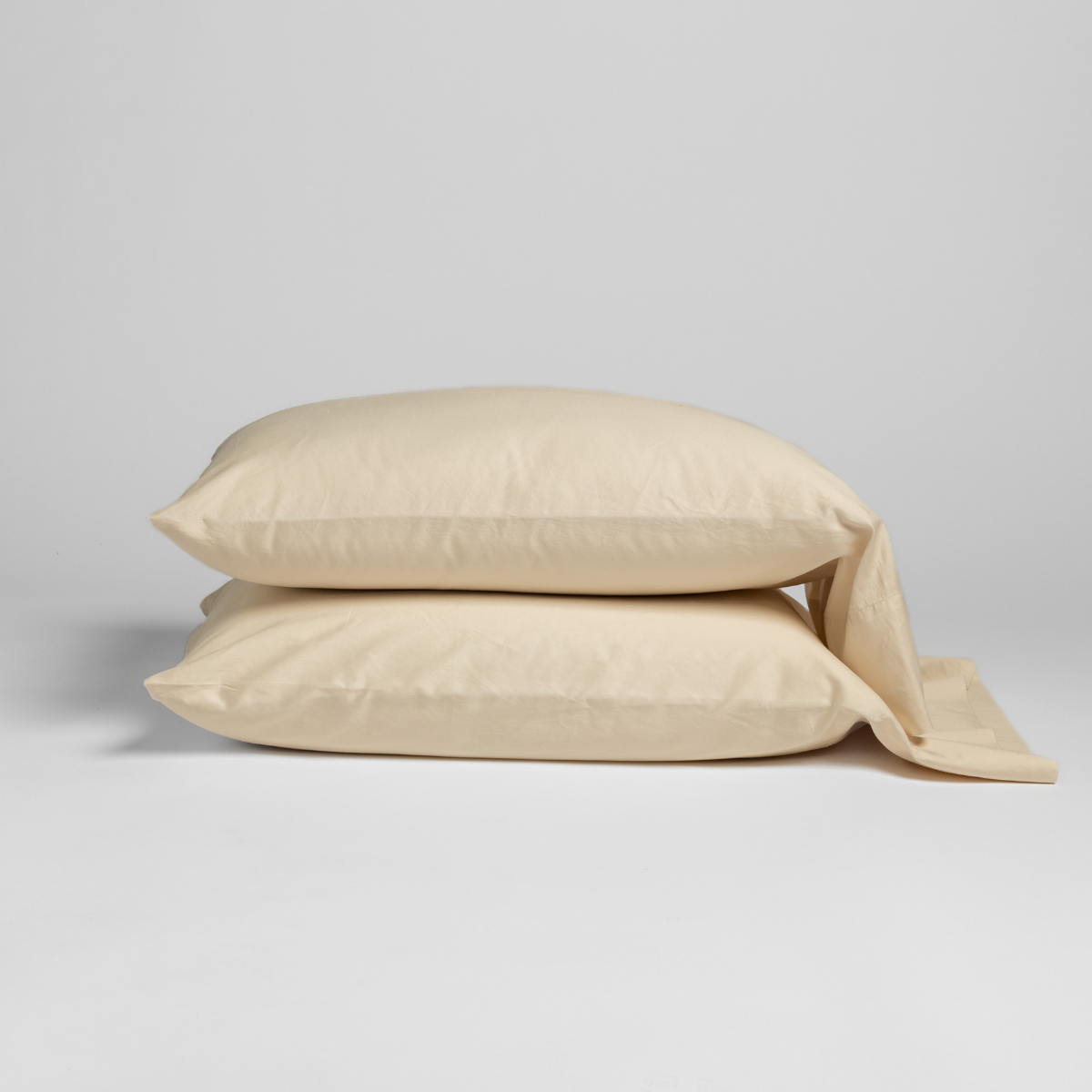 Two Bella Notte Bria pillowcases stacked in Natural, with a relaxed fabric tail draping to the side.