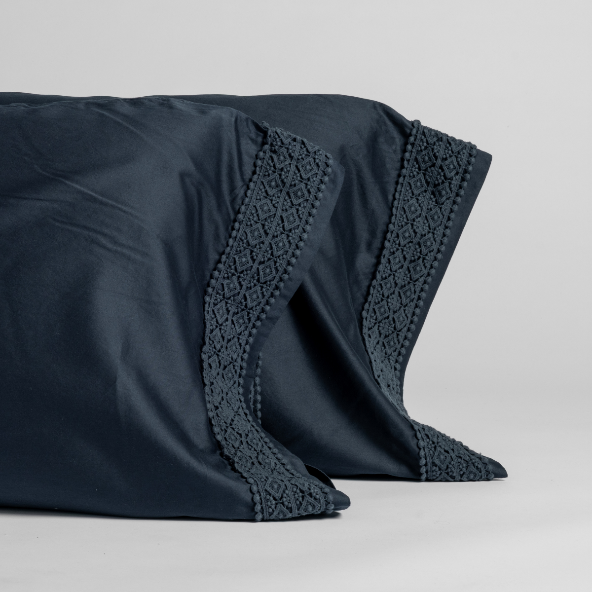 Close-up of two Slate Bria pillowcases showing diamond lace trim detail along the cuff edge.