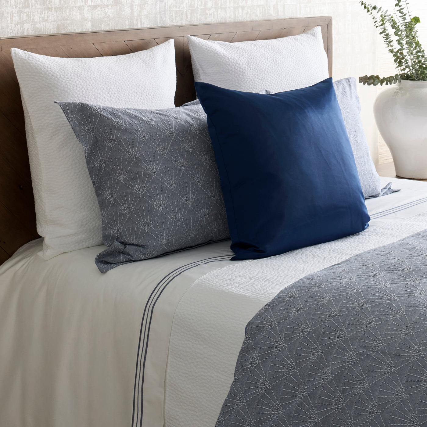 Ann Gish Bubble matelasse coverlet in grey styled on bed with navy and white accent pillows.