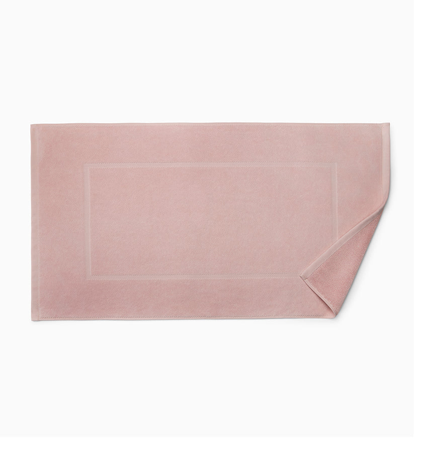 Blush terry tub mat with tonal woven border detail, corner folded back.
