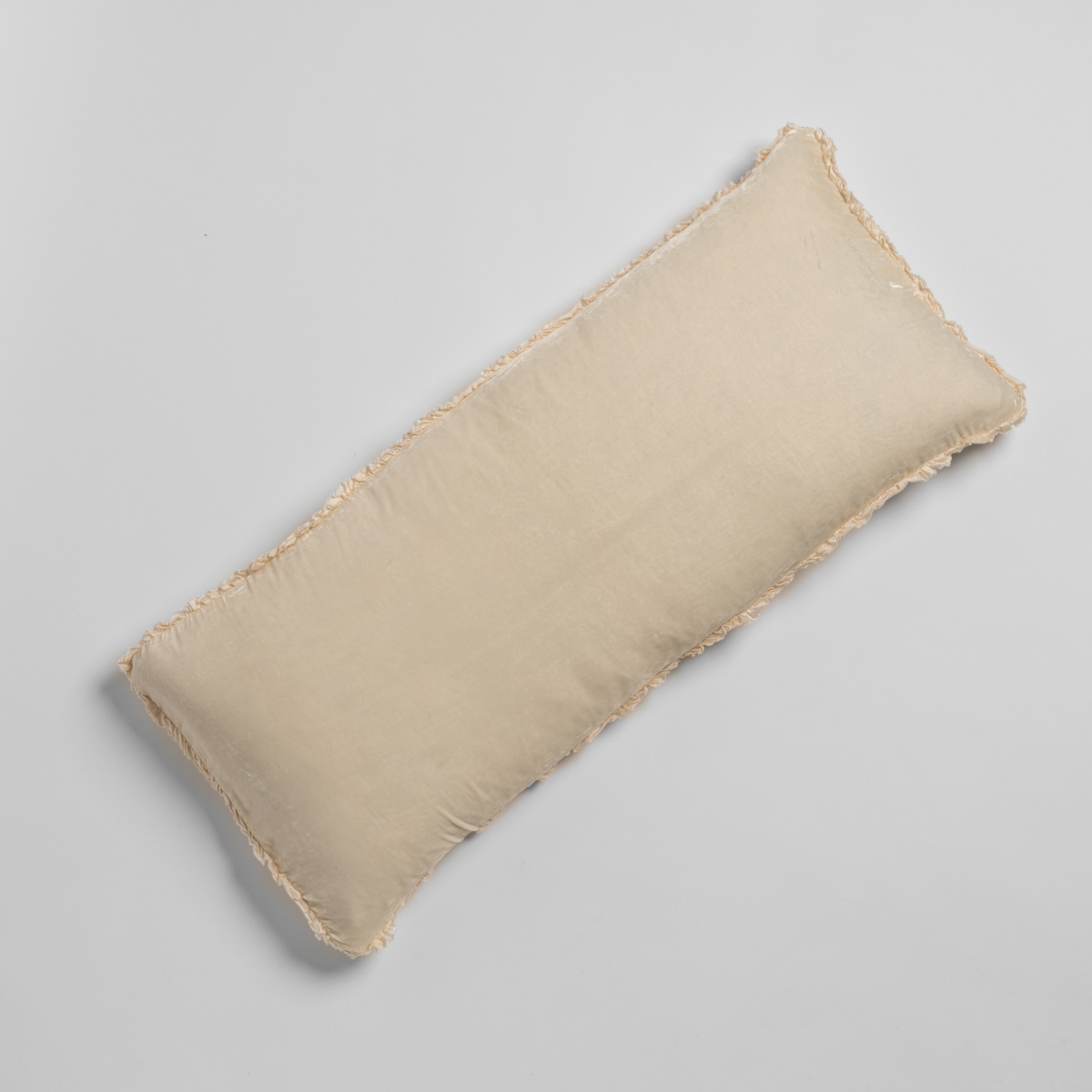 Overhead view of Crema Carmen throw pillow with fringe trim edges, rectangular shape.