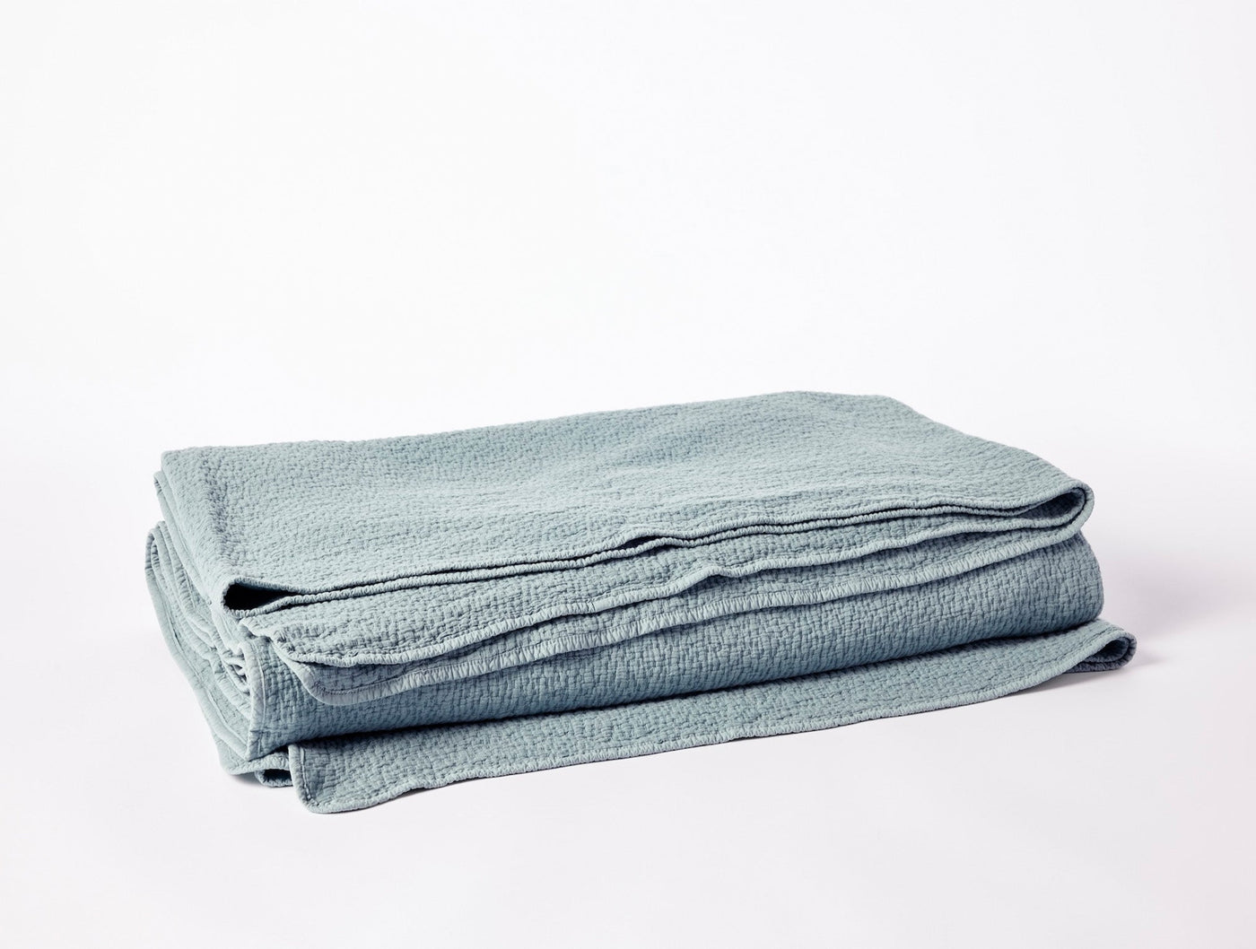 Coyuchi Cascade Matelassé blanket folded, showing seafoam textured weave and scalloped edge.