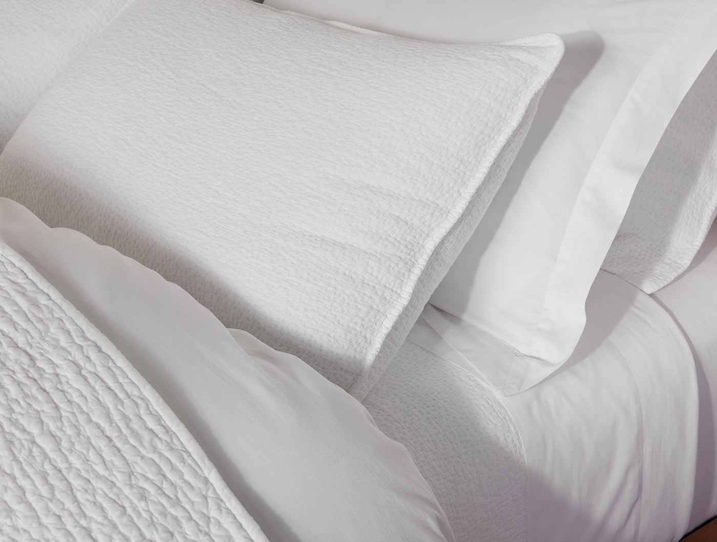 Close-up of white matelasse textured pillow sham layered over crisp white pillowcases on a styled bed.