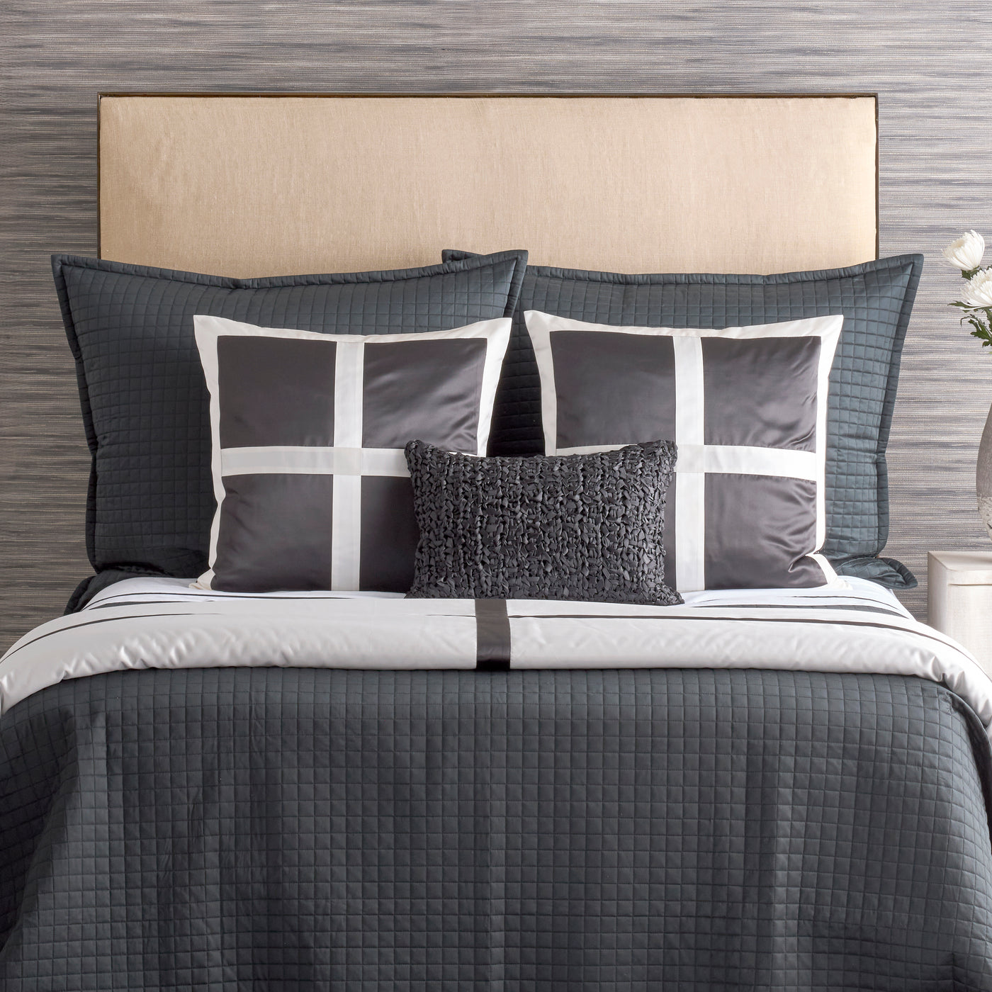 Ann Gish Cavendish pillow in charcoal, styled on a layered grey bed with quilted shams.