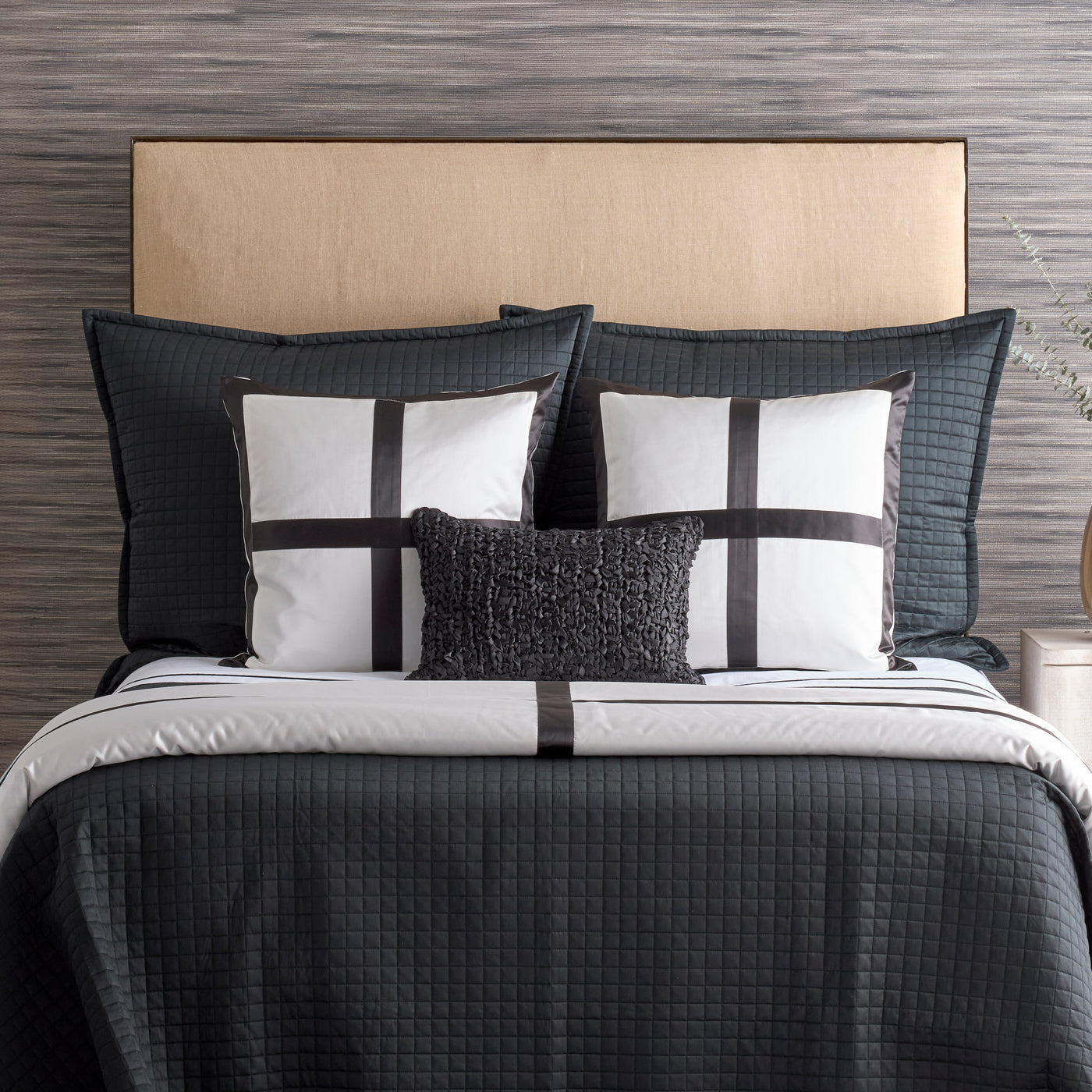 Ann Gish Cavendish pillow styled on a charcoal quilted bed with layered grey and white bedding.