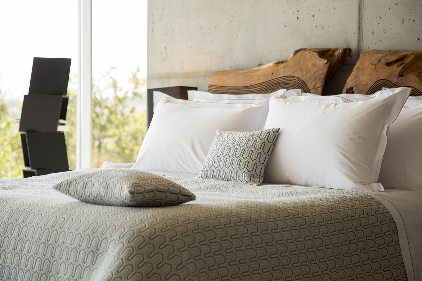 A close-up of a bed with white pillows and a textured grey throw, featuring Areo Pillowcase by Celso de Lemos available at Linen Society.