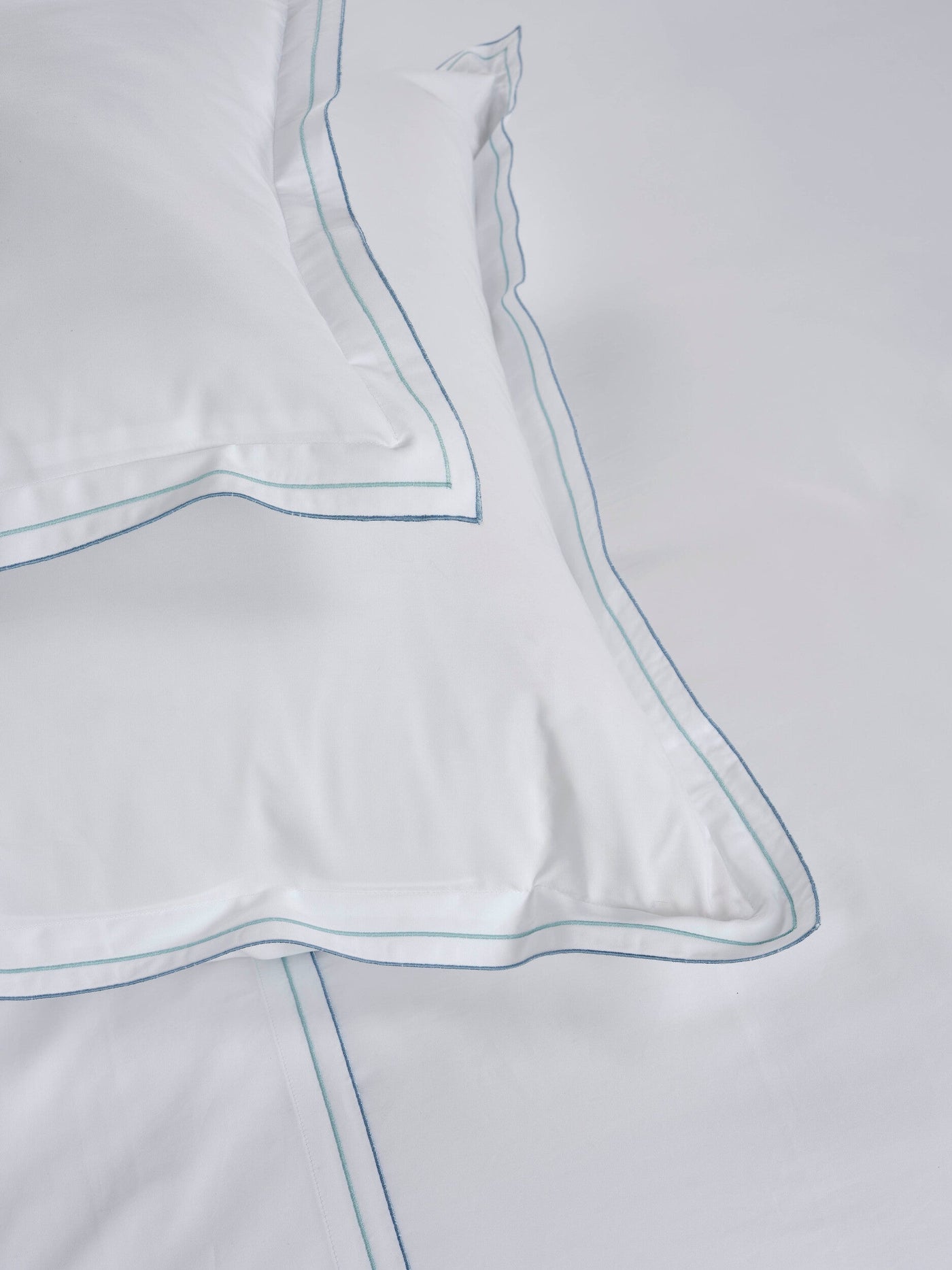 White pillow with blue and green stitching, featuring Areo Pillowcase by Celso de Lemos available at Linen Society.