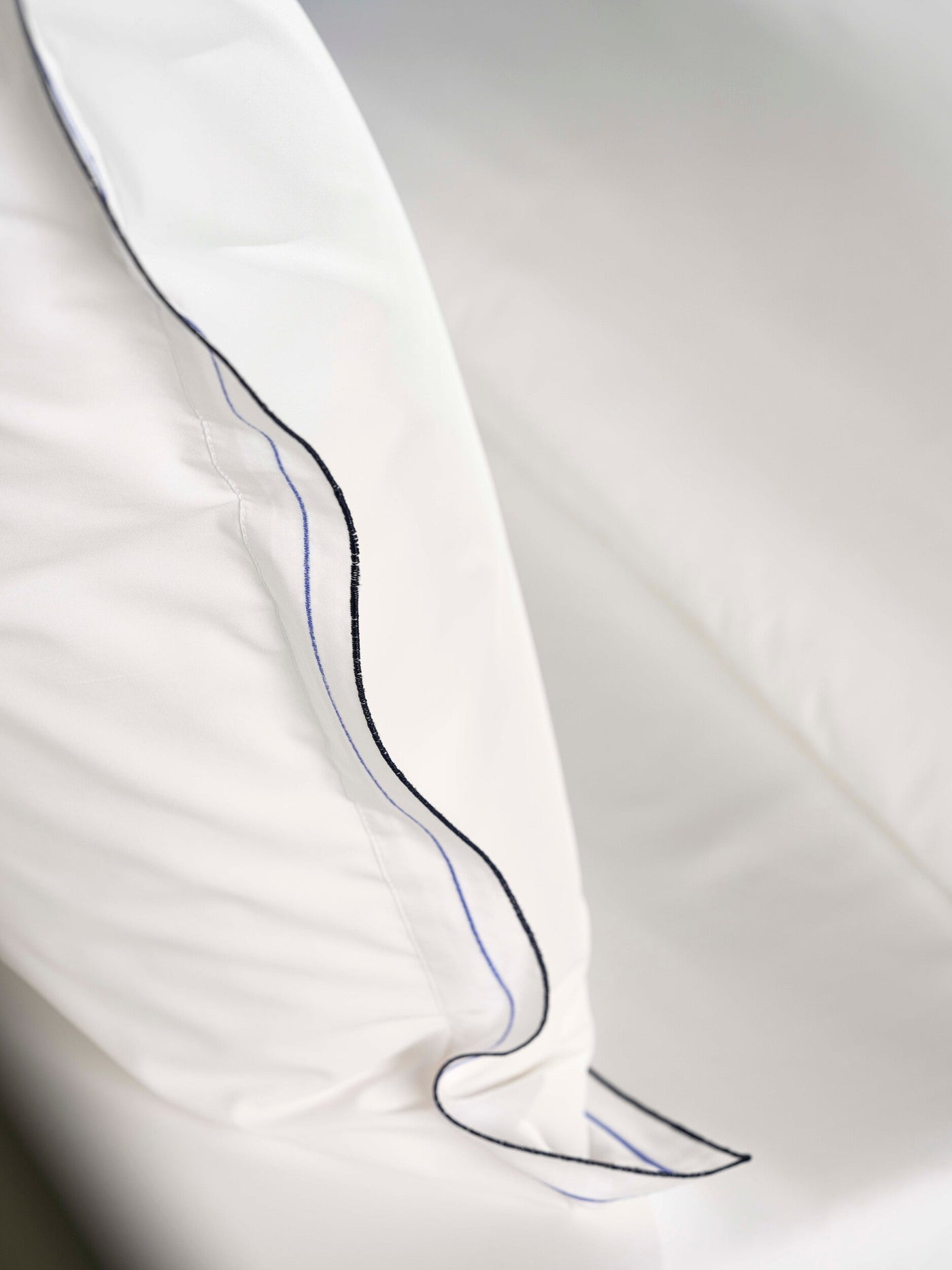 Close-up of white fabric with blue and black piping detail, featuring Areo Pillowcase by Celso de Lemos available at Linen Society.