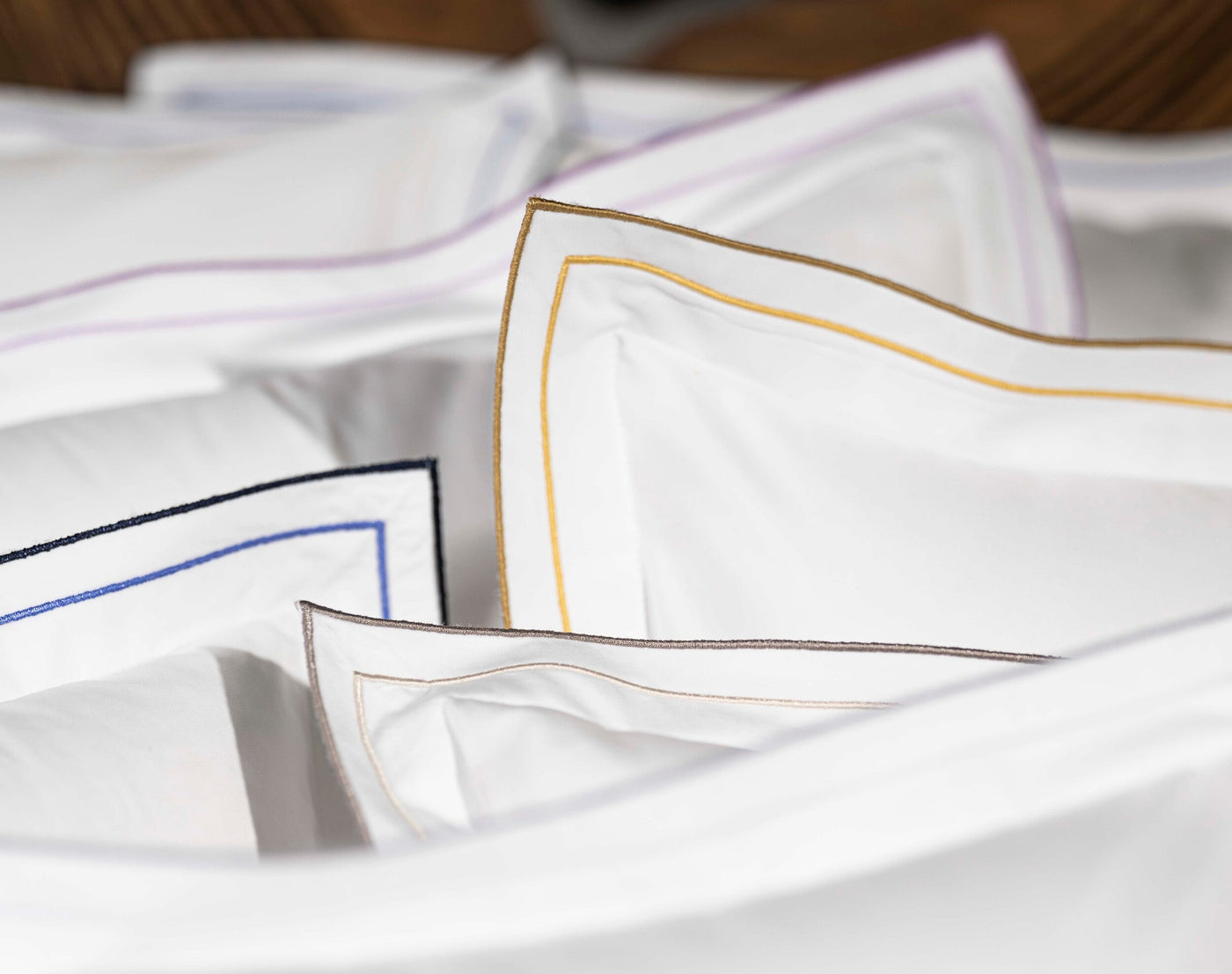 Close-up of white pillowcases with embroidered piping in gold, blue, and purple, featuring Areo Pillowcase by Celso de Lemos available at Linen Society.