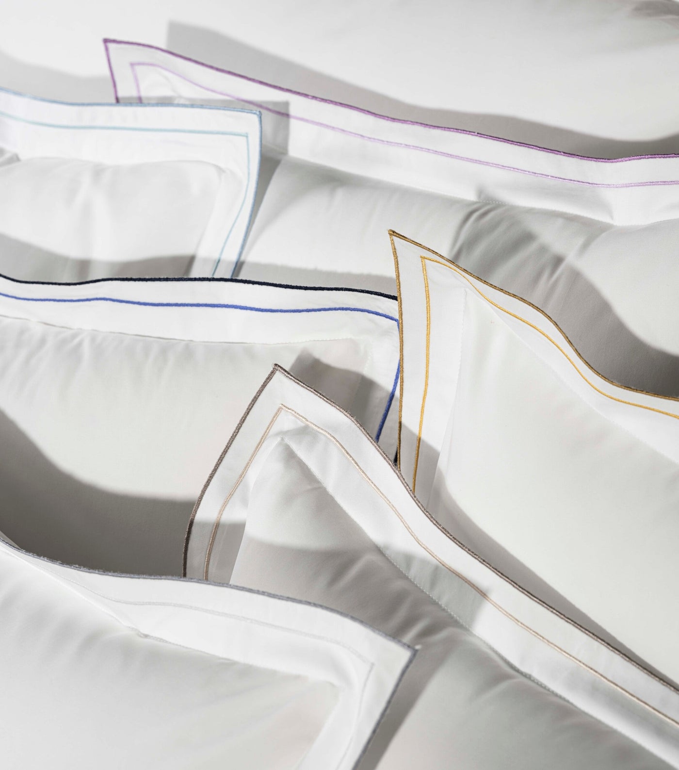 Close-up of white pillowcases with embroidered borders in purple, blue, gold, and grey threads, featuring Areo Pillowcases by Celso de Lemos available at Linen Society.