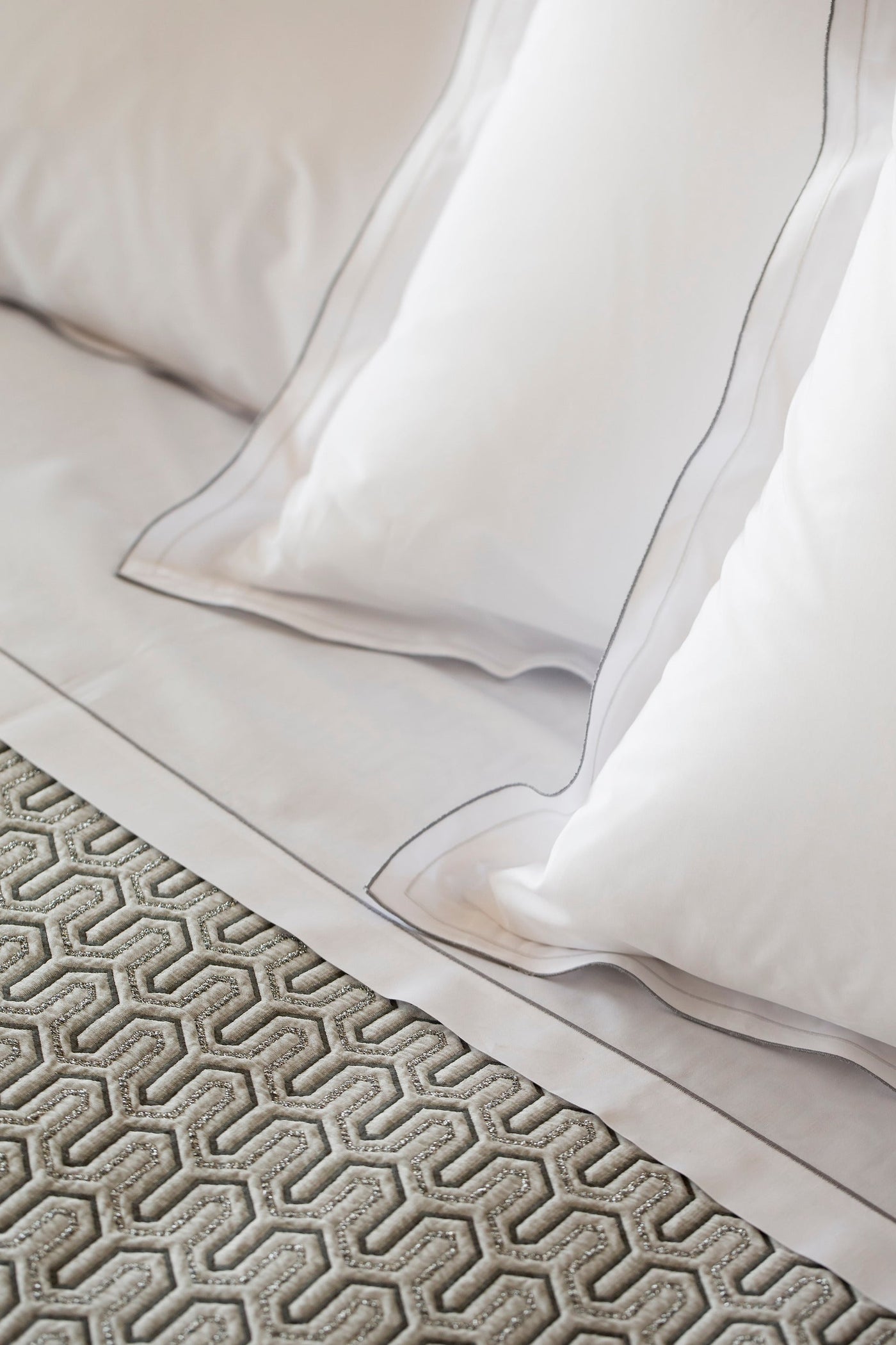 Close-up of white pillowcases with subtle grey stitching and a textured grey geometric throw, featuring Areo Pillowcase by Celso de Lemos available at Linen Society.