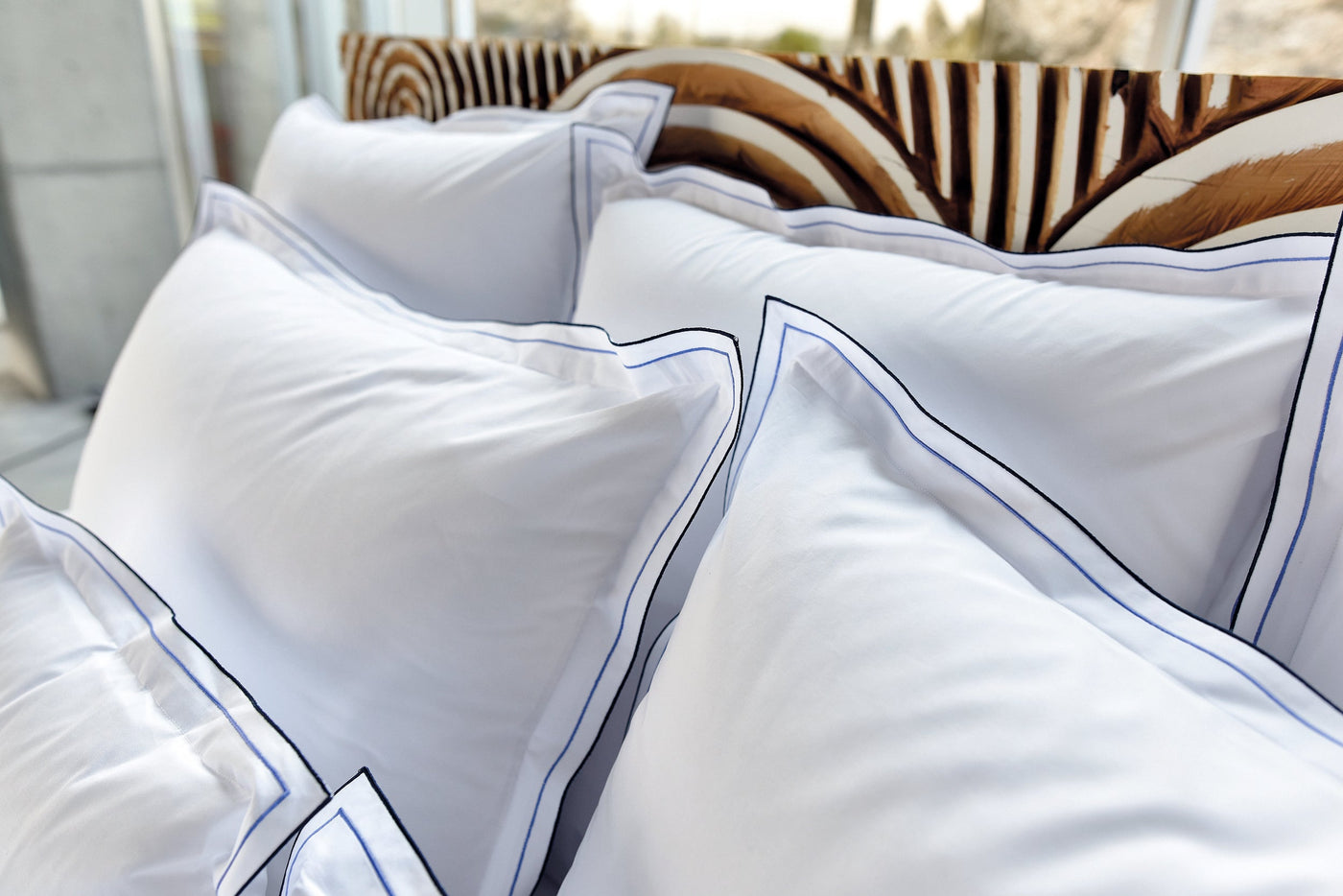 A close-up of white pillowcases with delicate blue and black piping. featuring Areo Pillowcase by Celso de Lemos available at Linen Society.