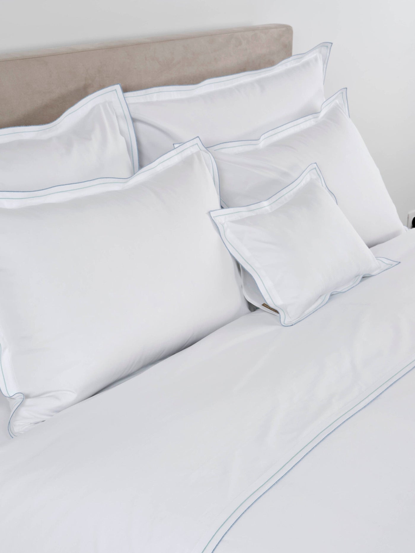 A white bedding ensemble with delicate blue stitching, featuring Areo Pillowcase by Celso de Lemos available at Linen Society.