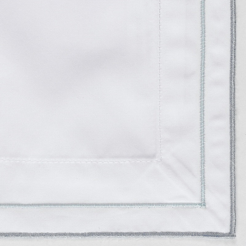 Close-up of white fabric with subtle stripes and light grey embroidery, featuring Areo Pillowcase by Celso de Lemos available at Linen Society.