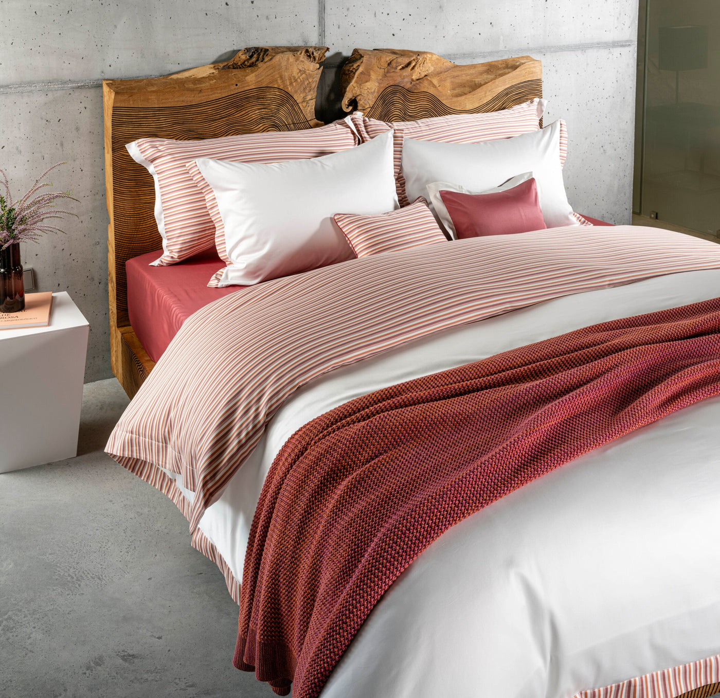 A neatly made bed with striped pillowcases and a coral knit throw blanket, featuring Baya Pillowcase by Celso de Lemos available at Linen Society.