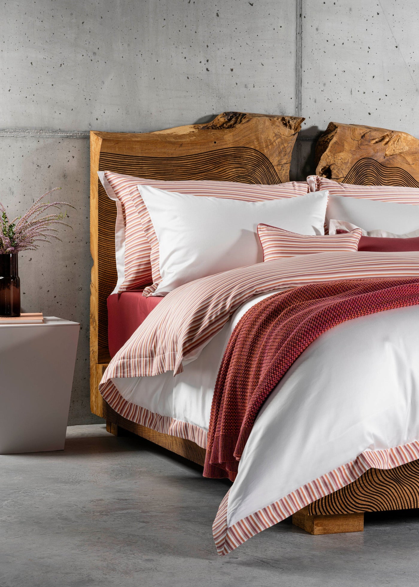 A neatly made bed with white bedding and coral-striped accents, featuring Baya Pillowcase by Celso de Lemos available at Linen Society.