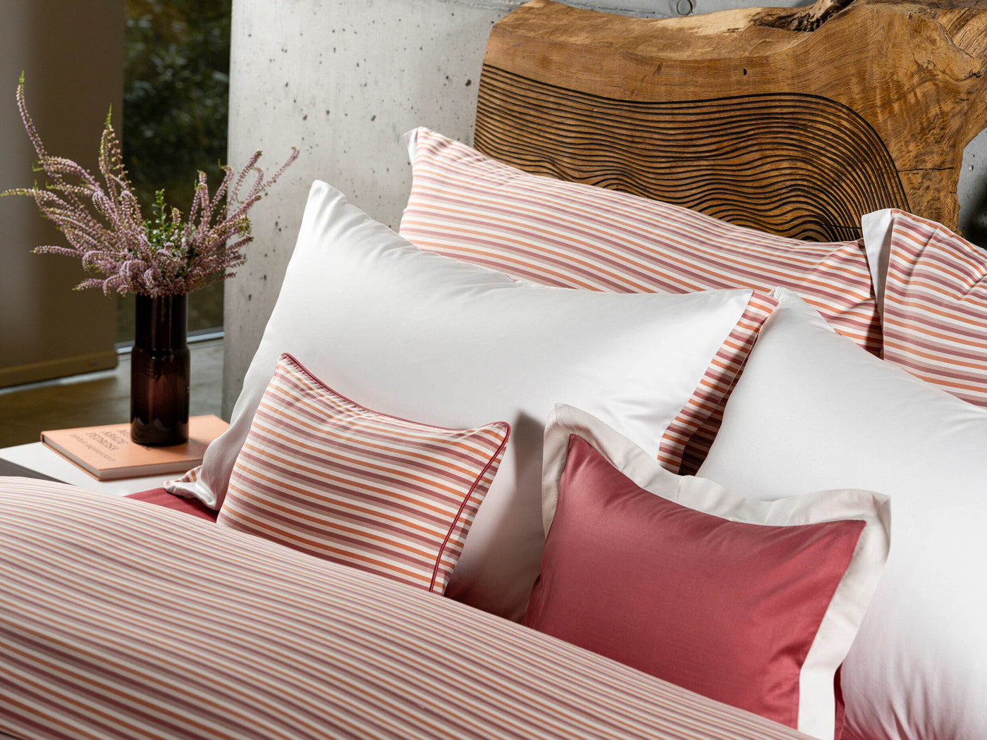 A bed is styled with white and striped pillowcases and a solid red accent pillow, featuring Baya Pillowcase by Celso de Lemos available at Linen Society.