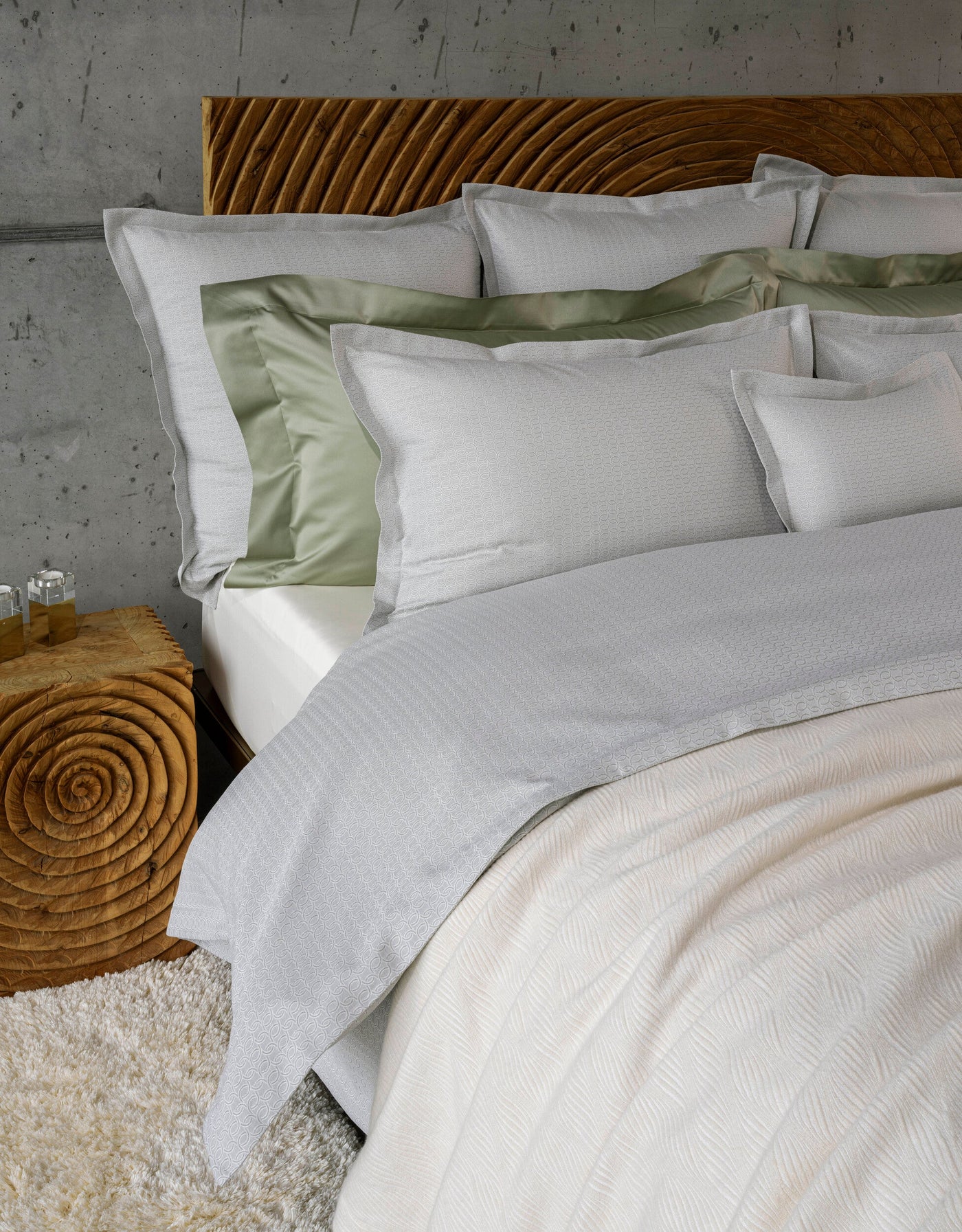 A bed styled with textured grey and sage green bedding on a wooden headboard, featuring Bijoux Pillowcase by Celso de Lemos available at Linen Society.