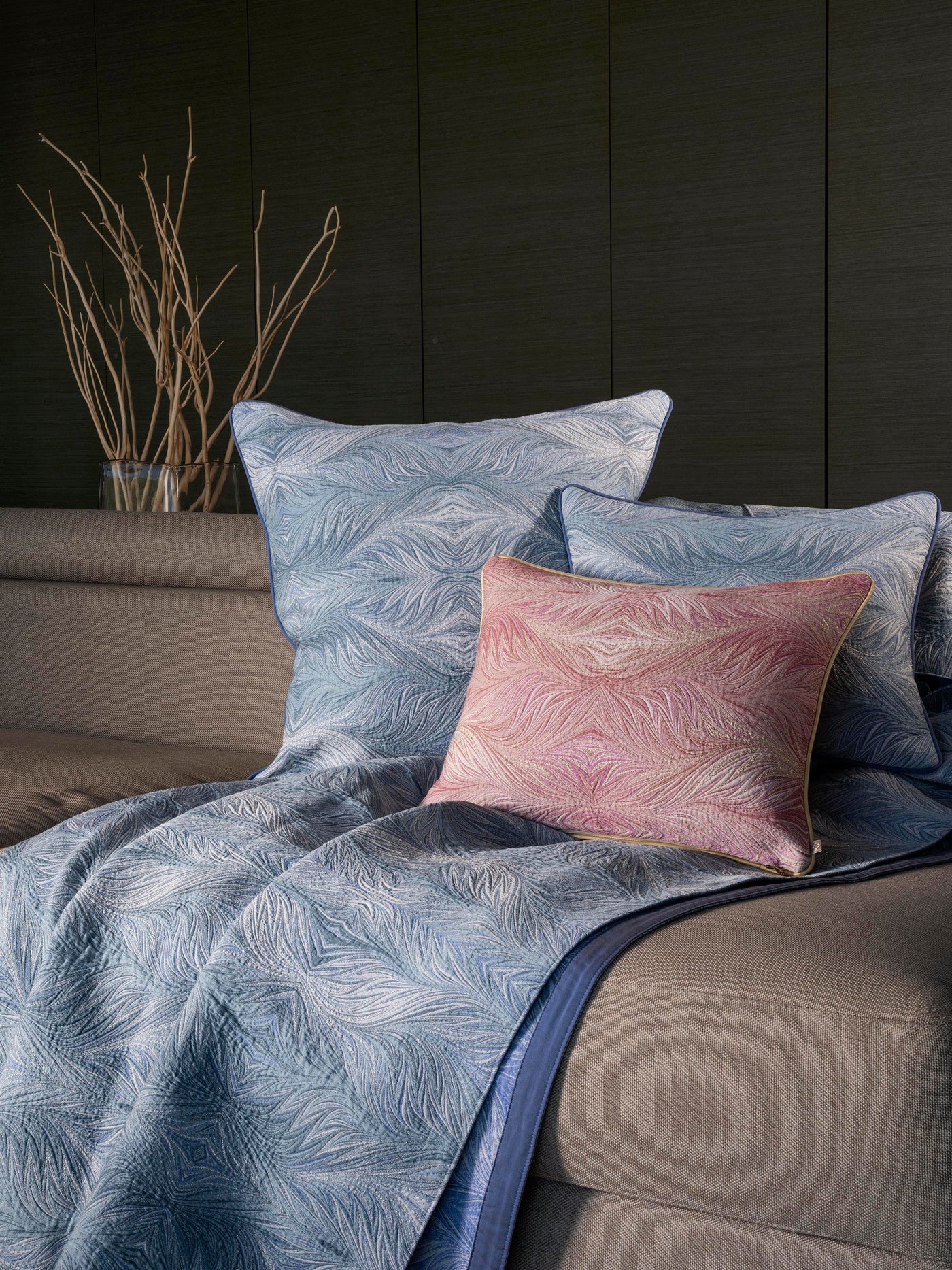 A pink pillow rests on blue patterned pillows and a blue throw on a sofa. featuring Boheme Pillow Cover by Celso de Lemos available at Linen Society.