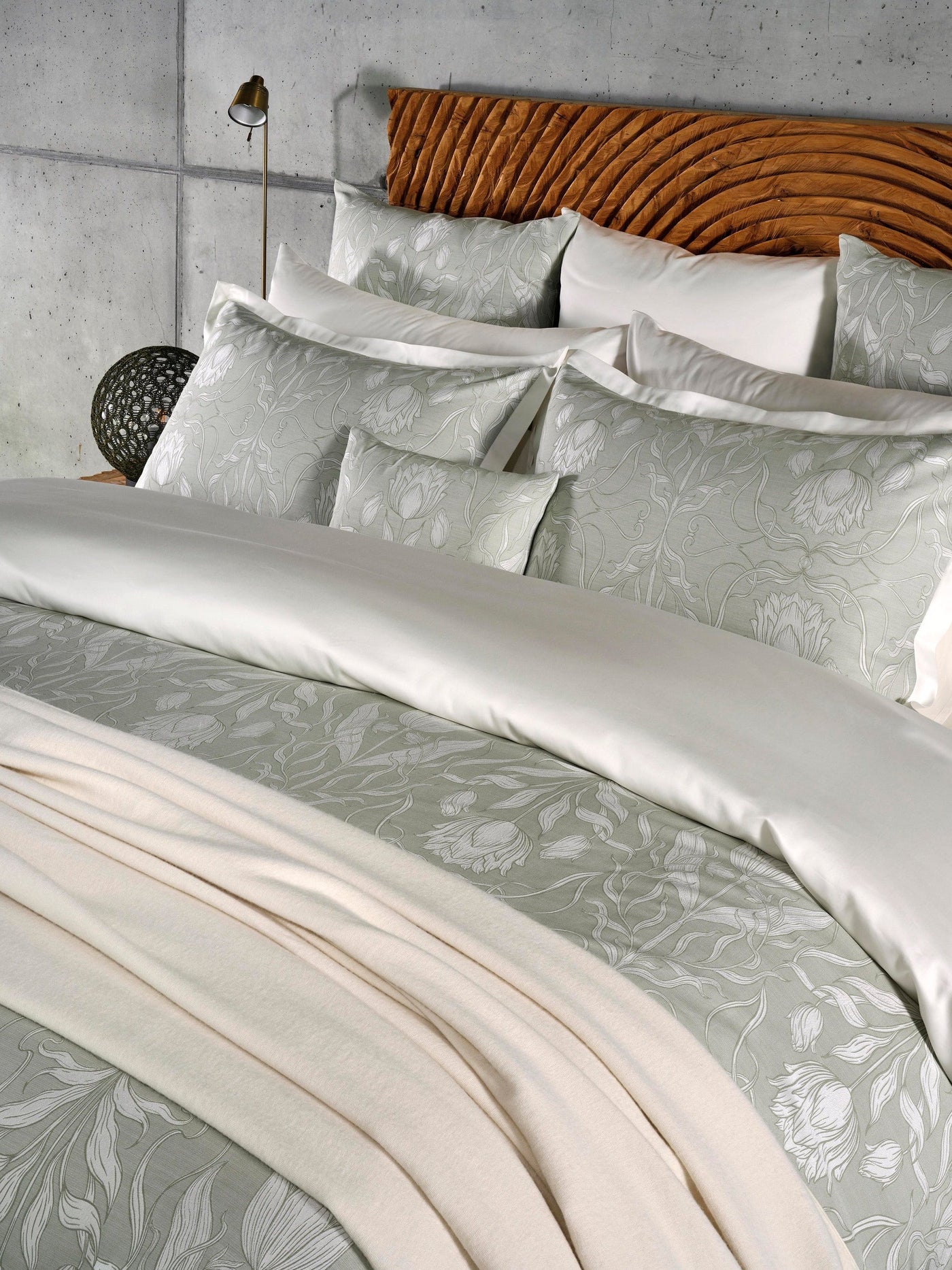 A neatly made bed displays a light grey duvet cover with a subtle floral pattern and white pillows, featuring Botanica Pillowcase by Celso de Lemos available at Linen Society.