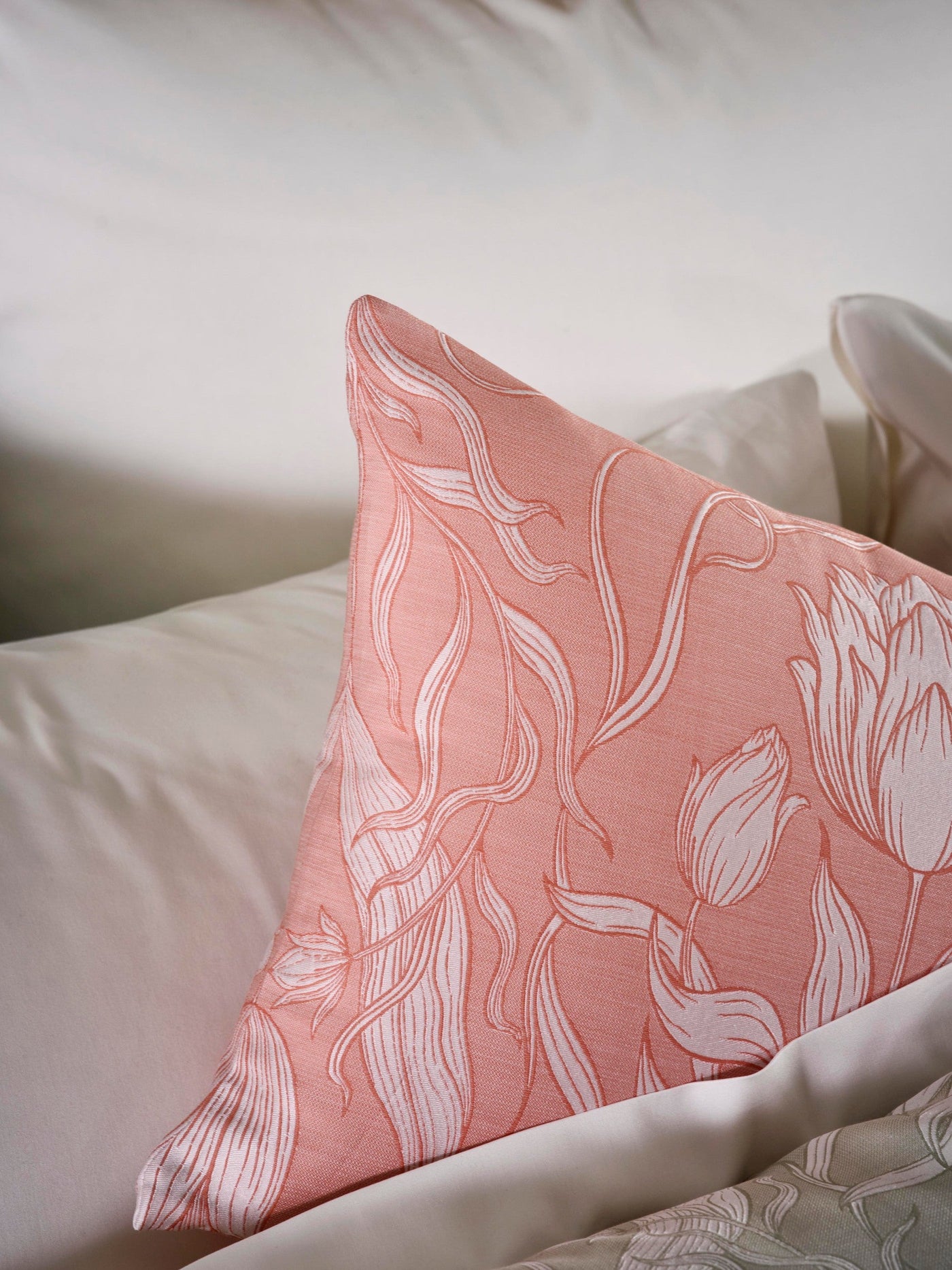 Close-up of a coral pillowcase with a white floral botanical pattern, resting on a white bed. featuring Botanica Pillowcase by Celso de Lemos available at Linen Society.
