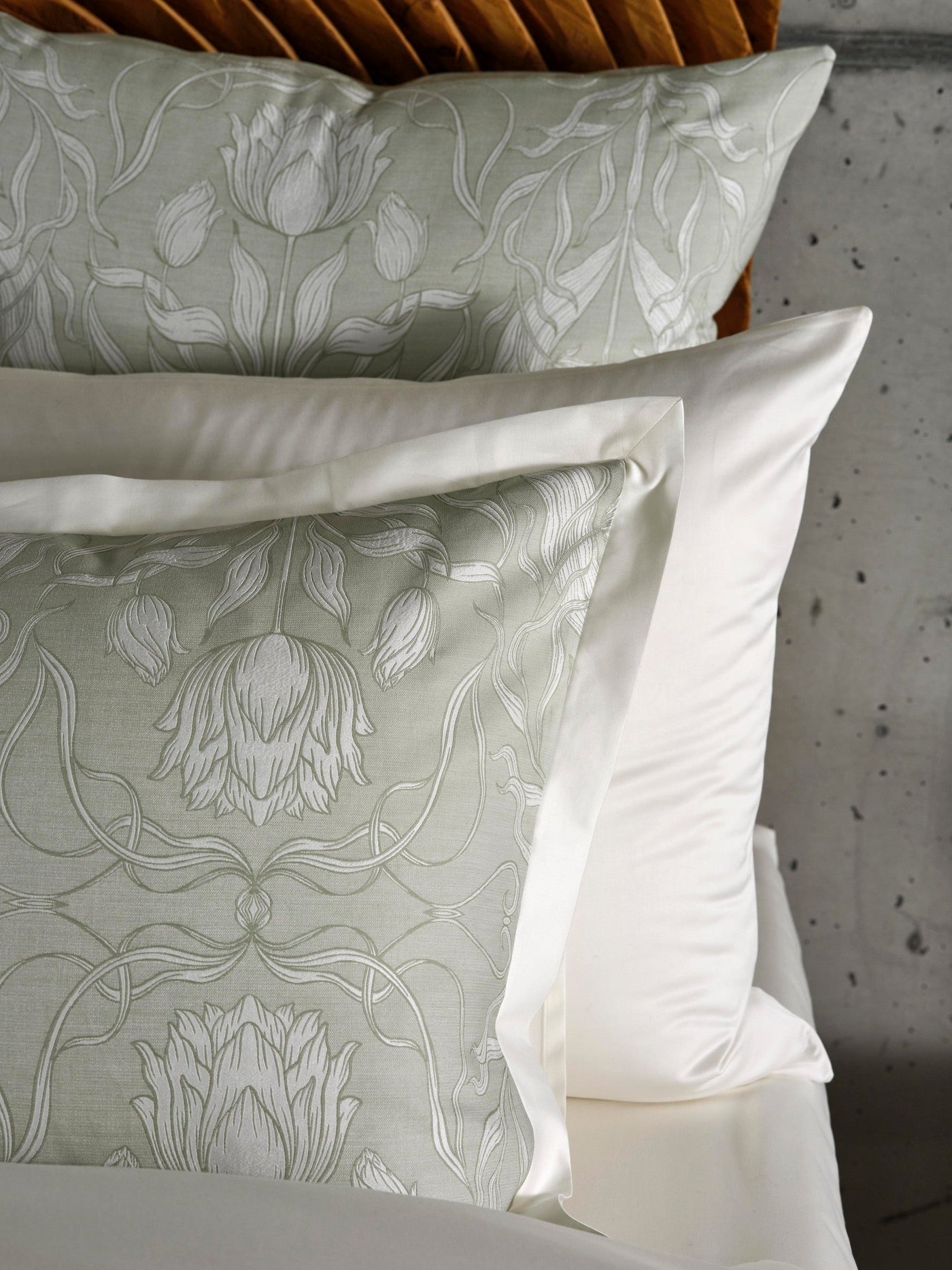 Soft green pillowcase with an intricate white floral damask pattern, layered with a white satin pillowcase, featuring Botanica Pillowcase by Celso de Lemos available at Linen Society.