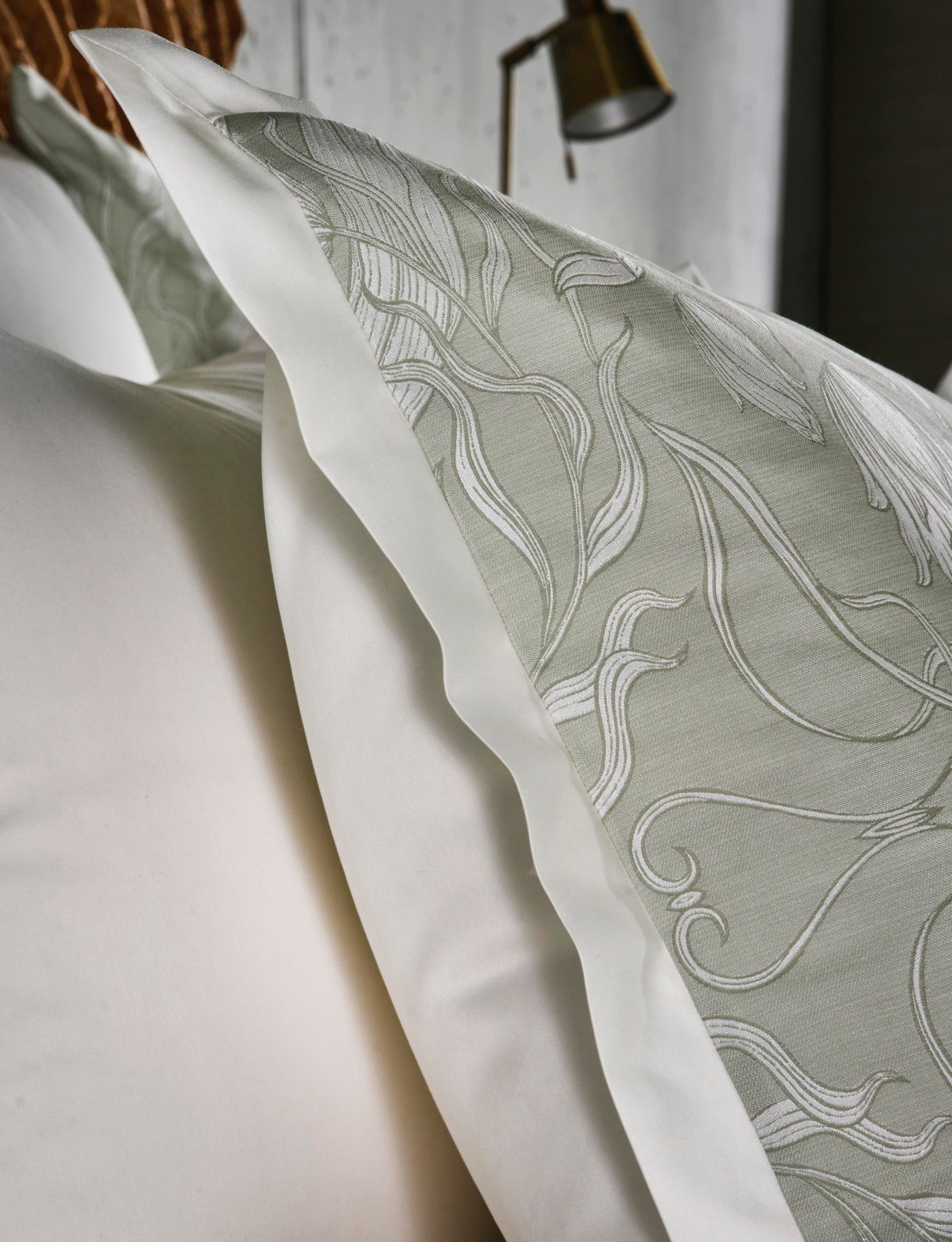 Close-up of white and pale green linens with a botanical pattern, featuring Botanica Pillowcase by Celso de Lemos available at Linen Society.
