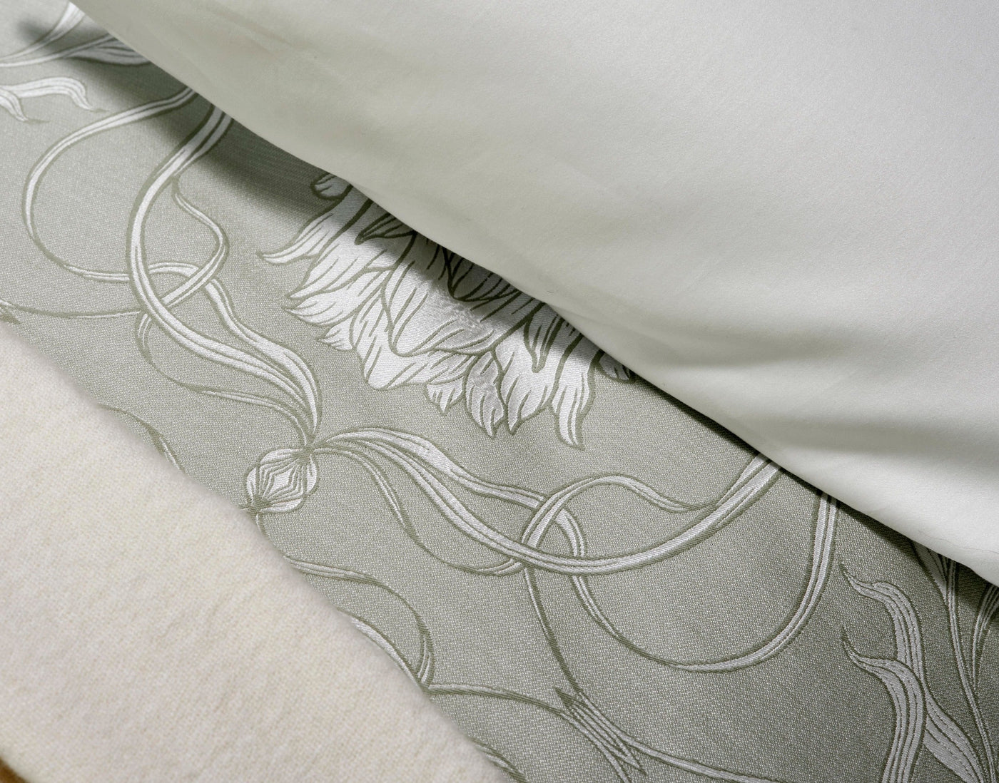 A close-up of a light sage green fabric with a subtle embossed white floral pattern and a soft ivory textured fabric, featuring Botanica Pillowcase by Celso de Lemos available at Linen Society.