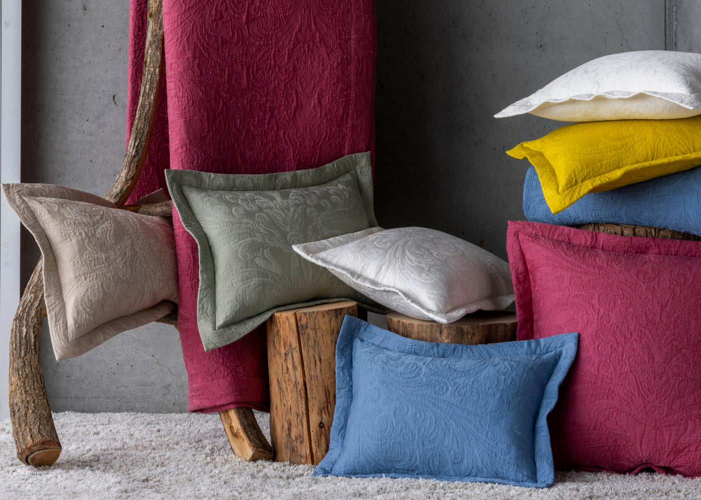 A rustic display of textured pillow covers in various colors like raspberry, sage green, cream, yellow, and blue. featuring Braga Pillow Cover by Celso de Lemos available at Linen Society.