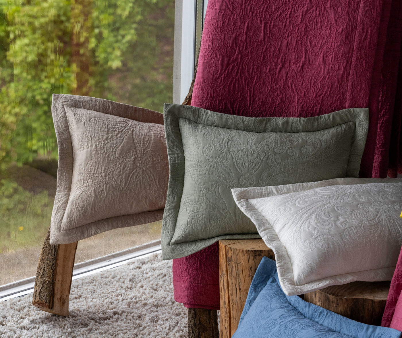 Several textured pillow covers in cream, sage green, and white are displayed, with a deep pink textured fabric behind them, featuring Braga Pillow Covers by Celso de Lemos available at Linen Society.