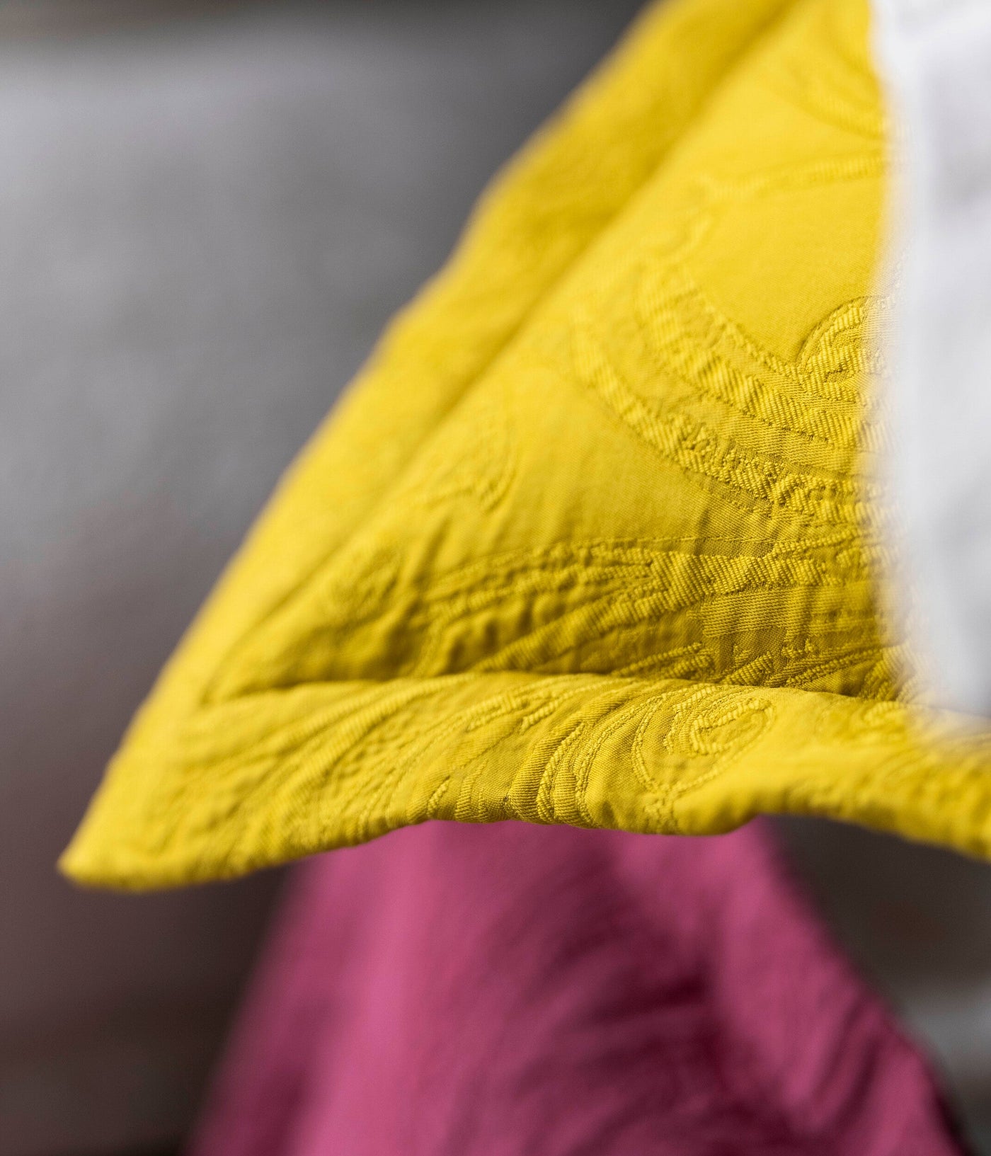 Close-up of a textured yellow cover with a subtle weave pattern, draped over a fuchsia fabric, featuring the Braga Pillow Cover by Celso de Lemos available at Linen Society.