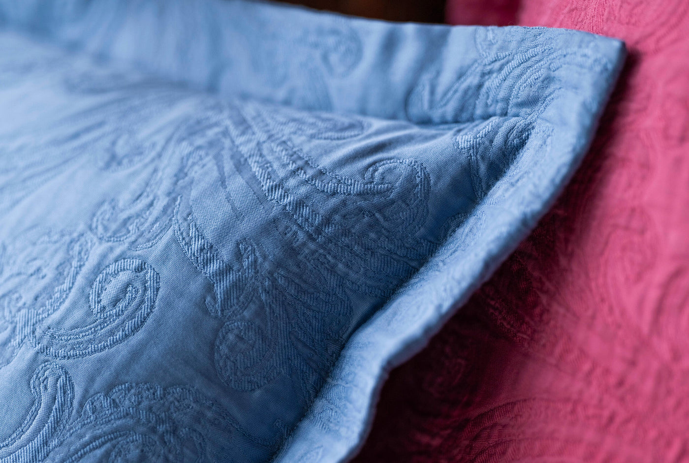 Close-up of a textured blue pillow cover with an embossed paisley pattern, alongside a pink textured textile, featuring Braga Pillow Cover by Celso de Lemos available at Linen Society.