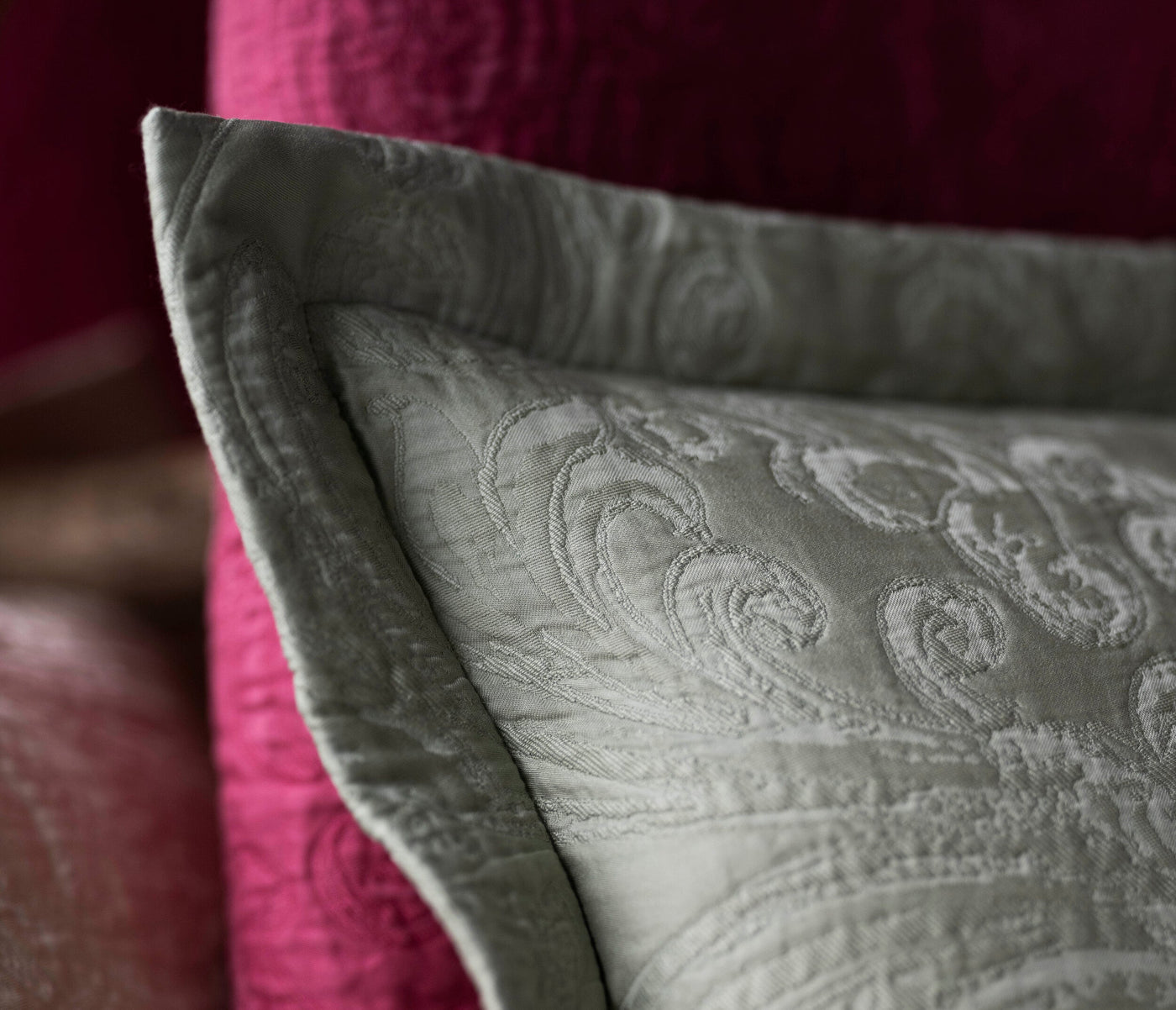 Close-up of a light green pillow cover with an embroidered damask pattern, set against a blurred fuchsia background, featuring Braga Pillow Cover by Celso de Lemos available at Linen Society.