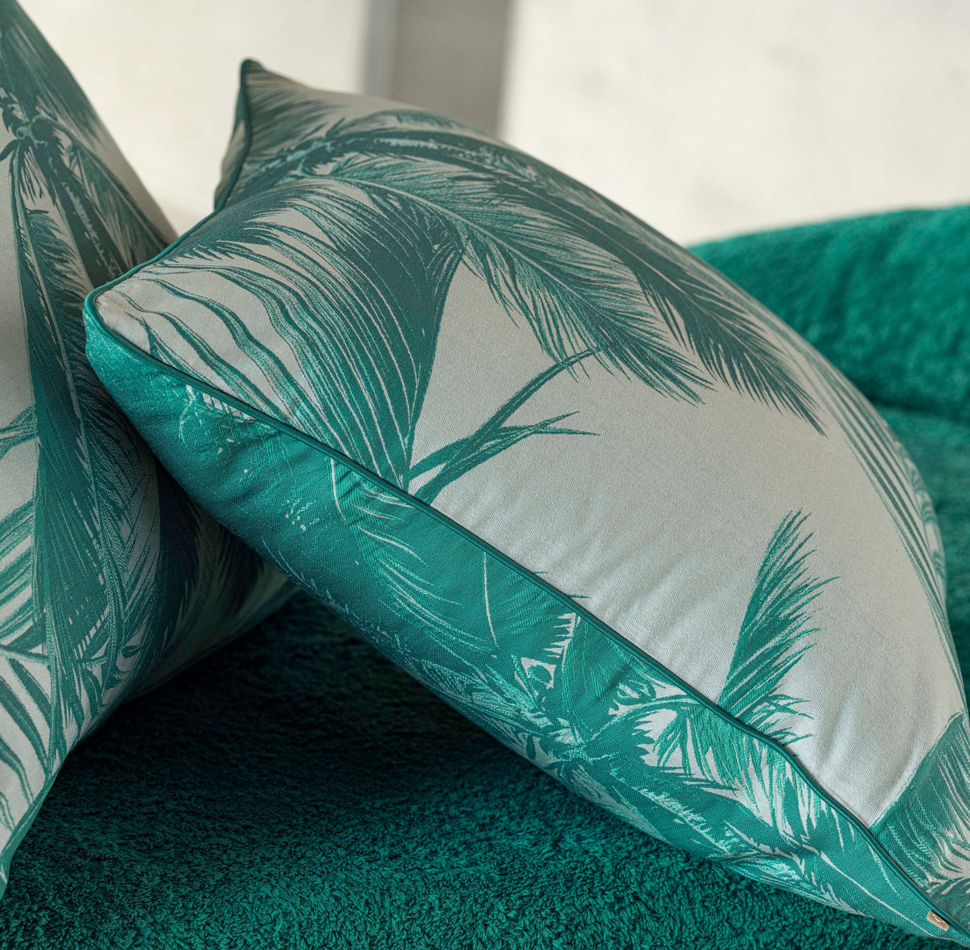Two plush green decorative pillows with a white palm leaf pattern are displayed on a textured green sofa, featuring Cabo Verde Pillow Cover by Celso de Lemos available at Linen Society.