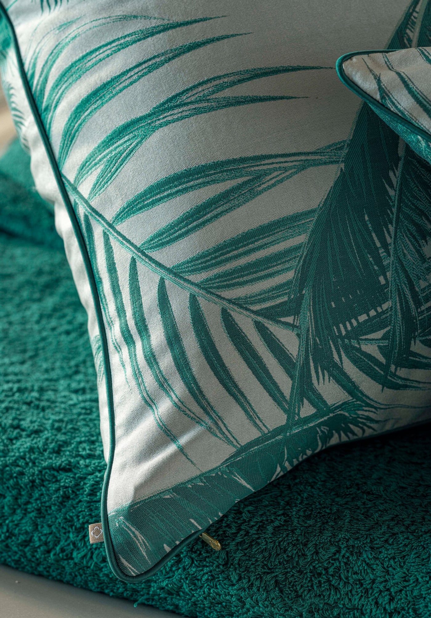 A close-up of a pillow with a tropical leaf pattern in teal and white. featuring Cabo Verde Pillow Cover by Celso de Lemos available at Linen Society.
