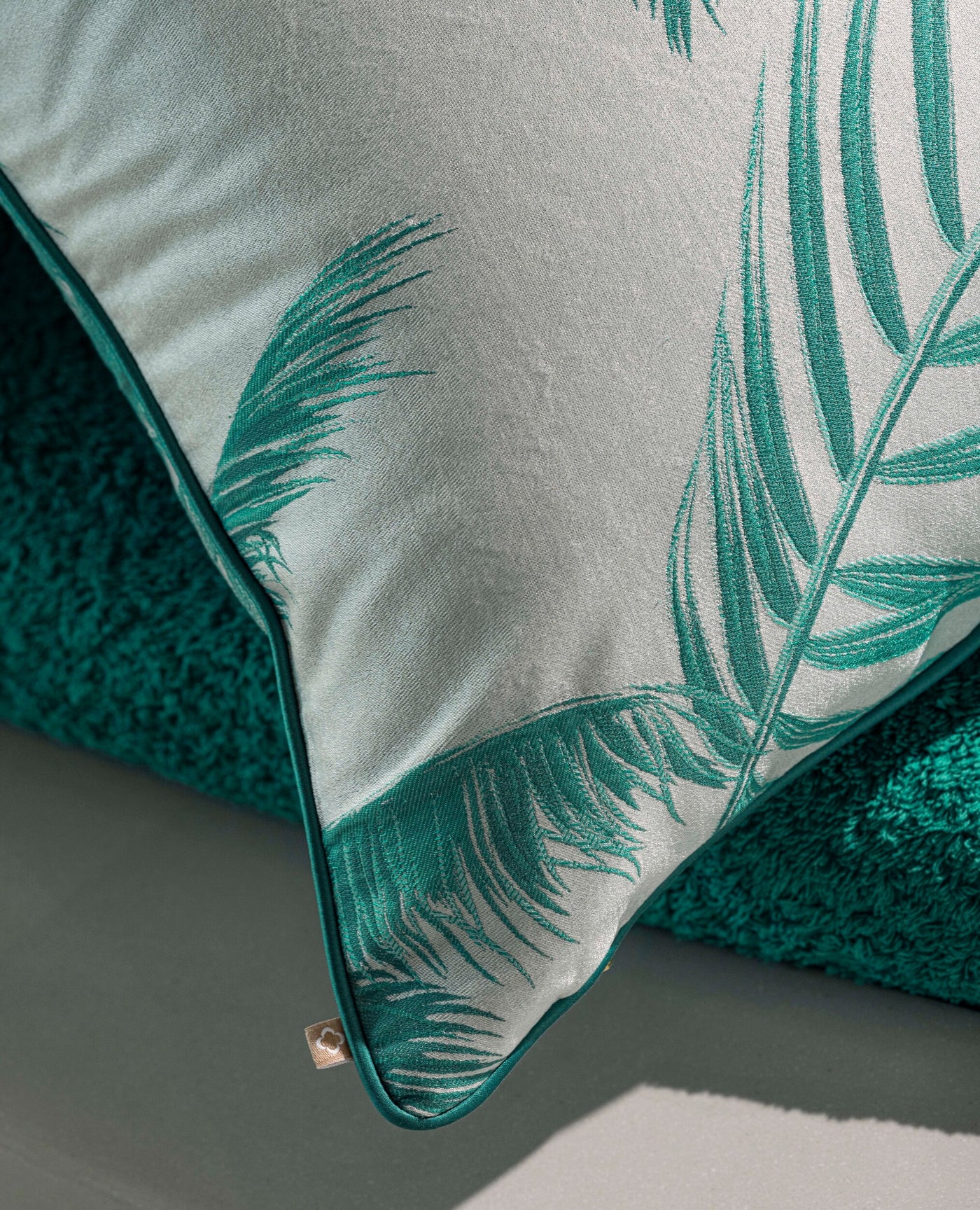 Close-up of a pale green pillow with an embroidered tropical leaf pattern in deep teal, featuring the Cabo Verde Pillow Cover by Celso de Lemos available at Linen Society.