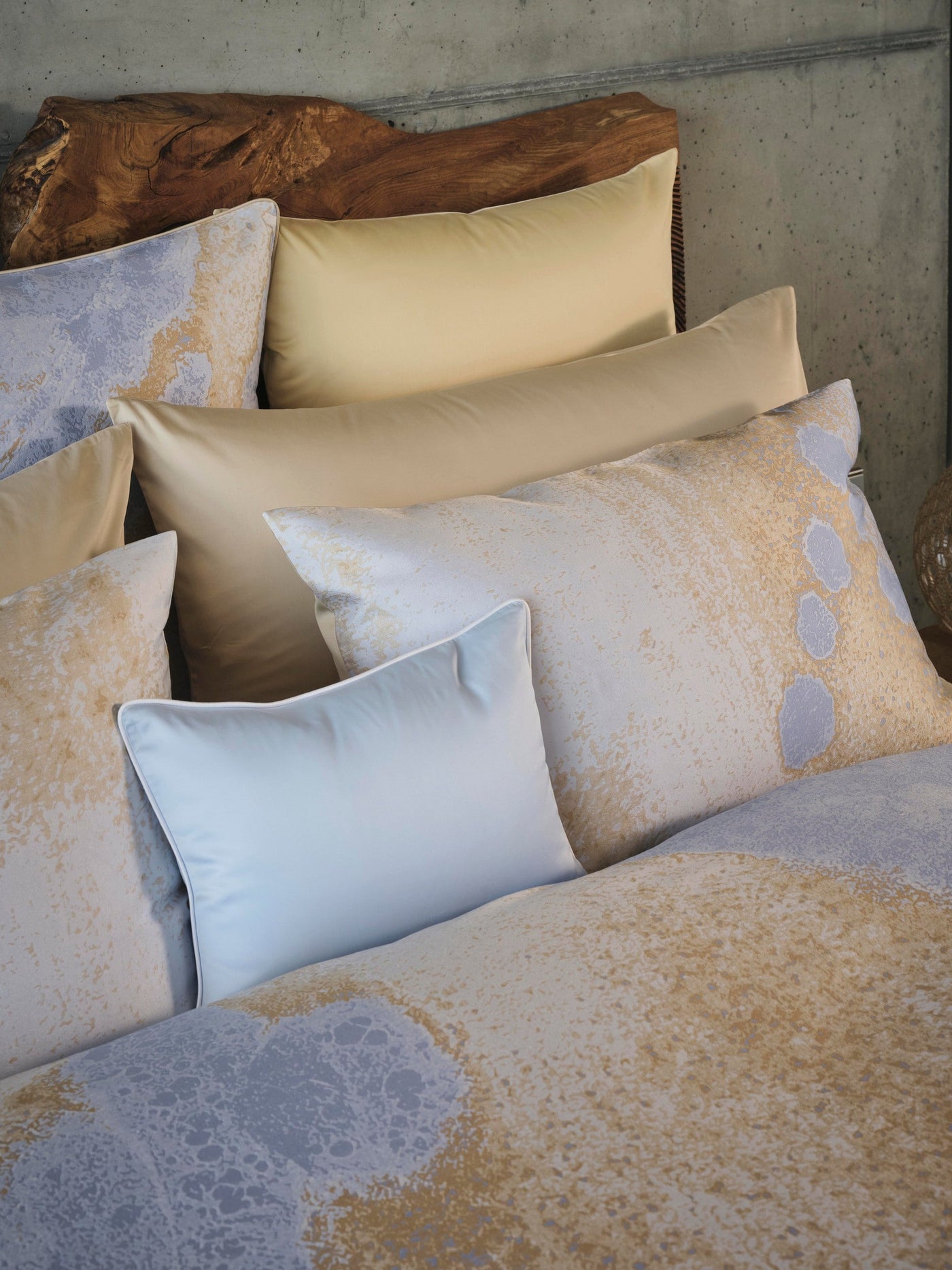 A bed layered with patterned pillowcases in beige, gold, and blue hues, featuring the Callisto Pillowcase by Celso de Lemos available at Linen Society.